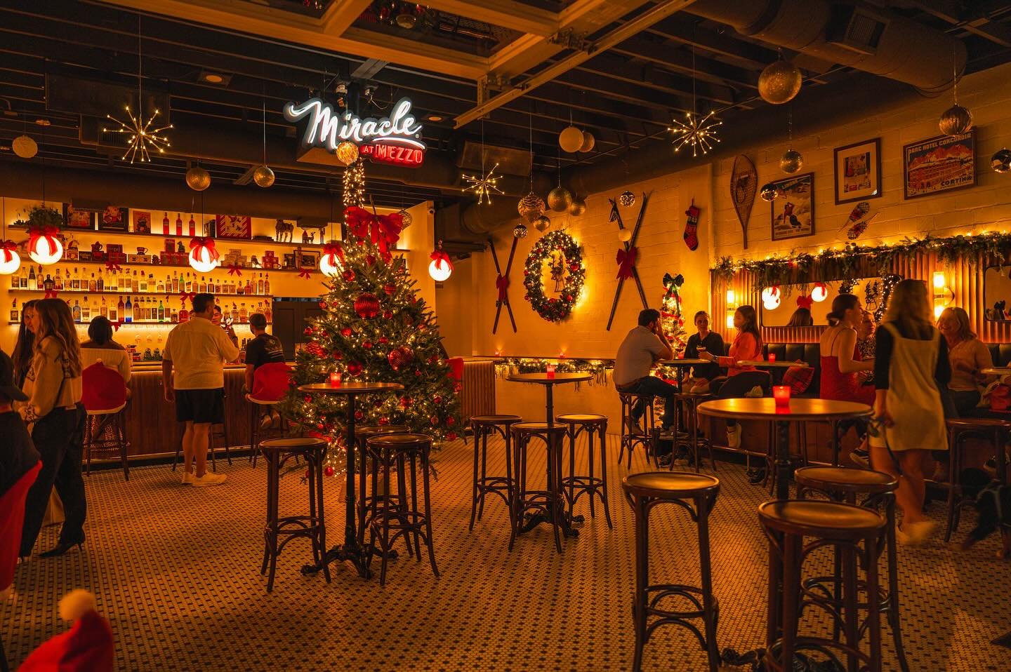Interior of the Miracle at Mezzo Christmas pop-up bar in downtown St. Pete featuring festive decorations, wreaths, a Christmas tree, and guests enjoying holiday cocktails.