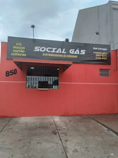 Fachada de loja "Social Gás" com oferta de gás, bebidas, carvão e essências, fachada vermelha, números de telefone para entregas.