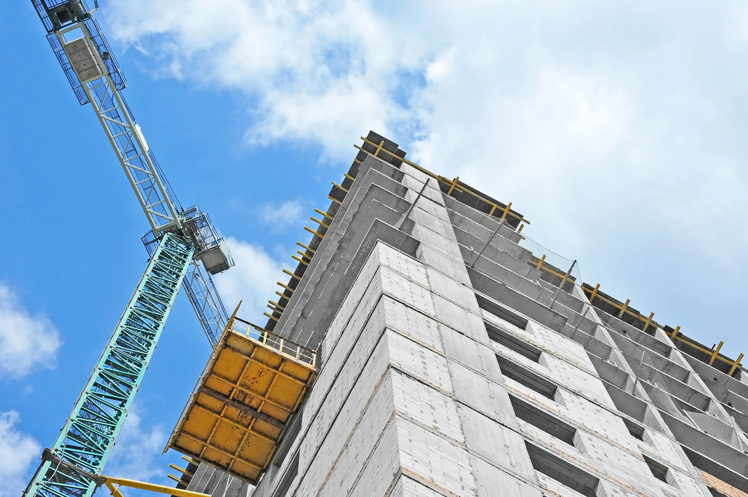 Construction site with a tall building under development and a tower crane against a blue sky with clouds.