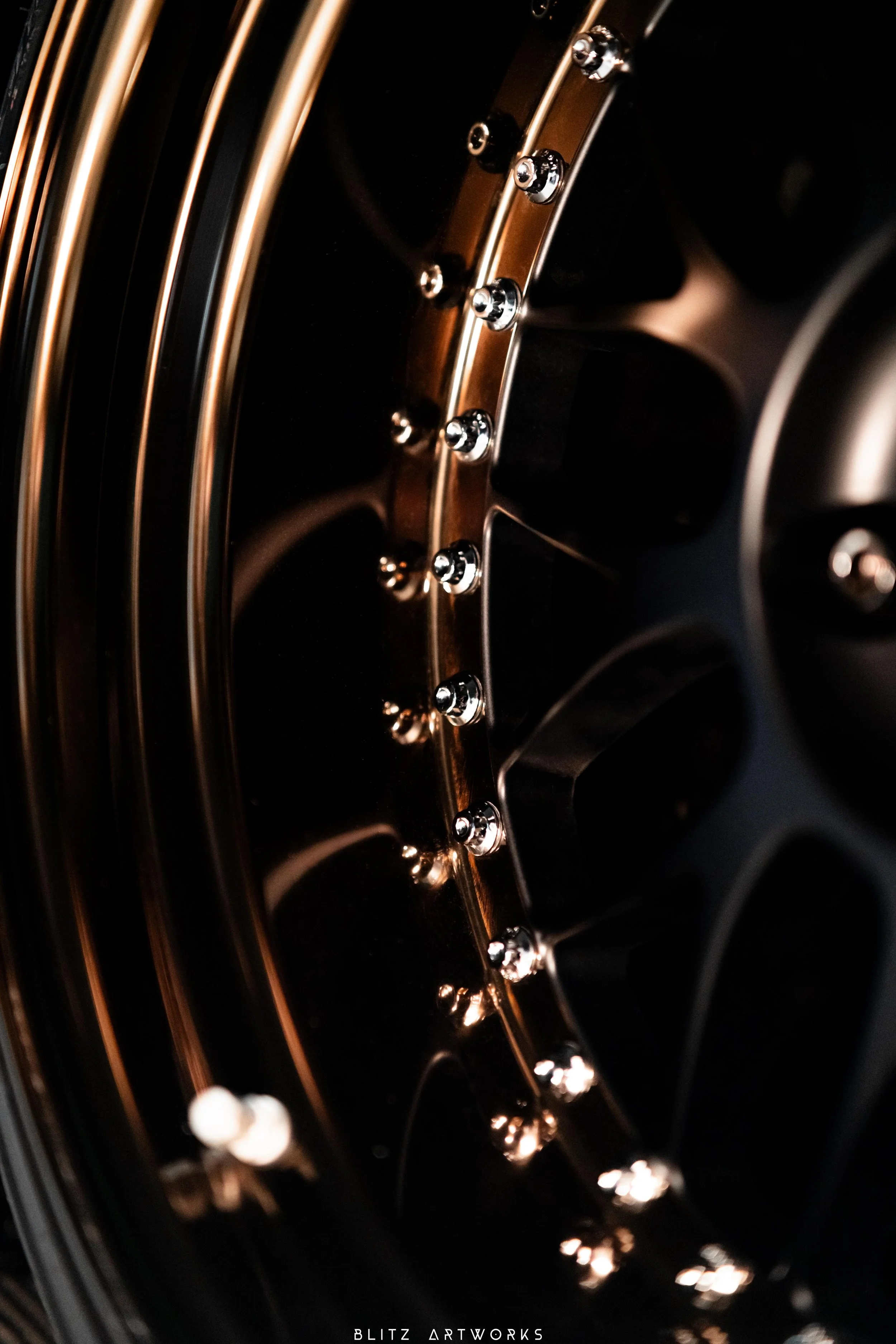 Détail d'une roue de voiture sportive avec des boulons chromés brillants et des jantes noires avec des cercles dorés