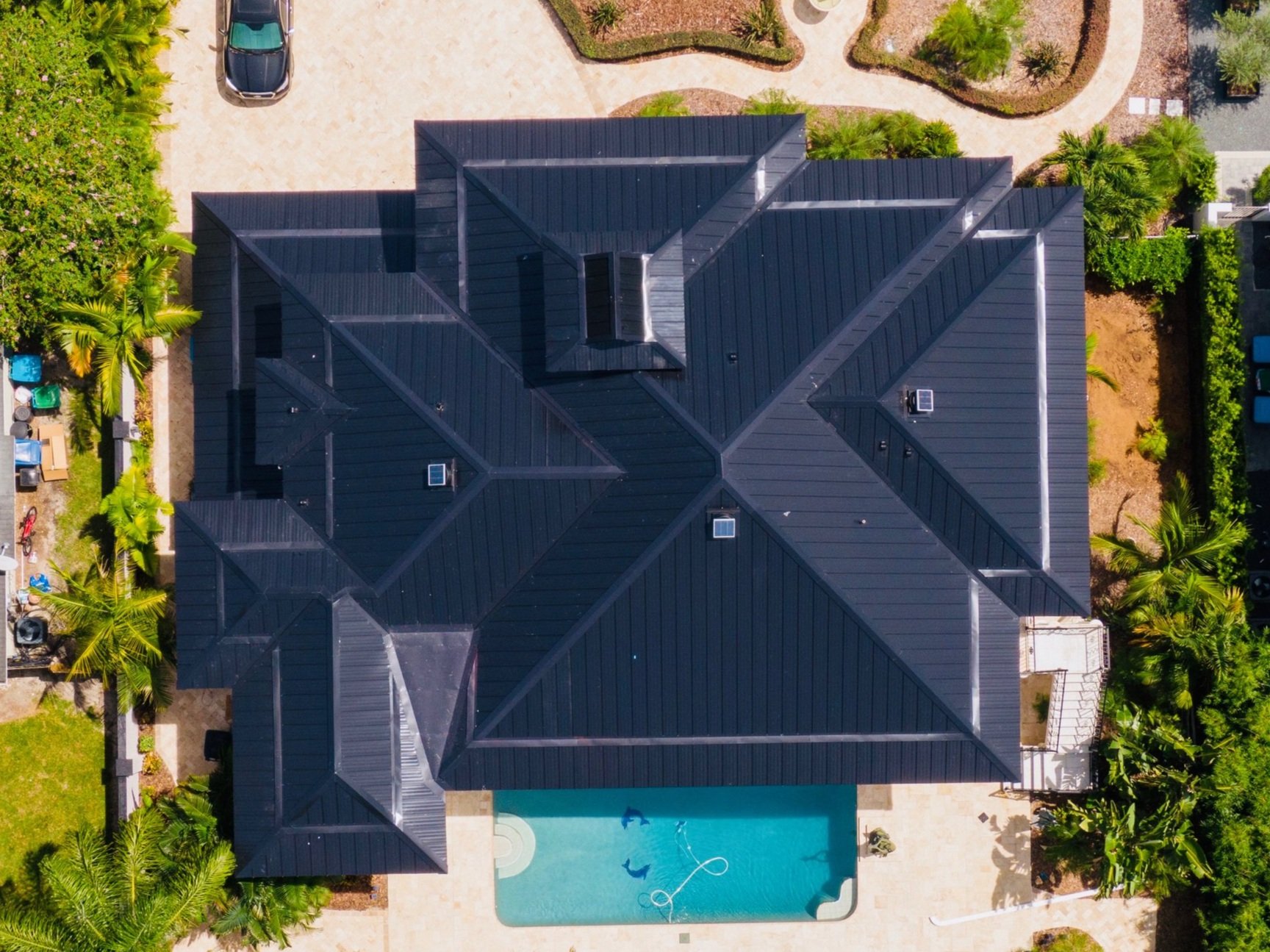 Aerial view of a luxury home with a black standing seam metal roof and pool in Florida.