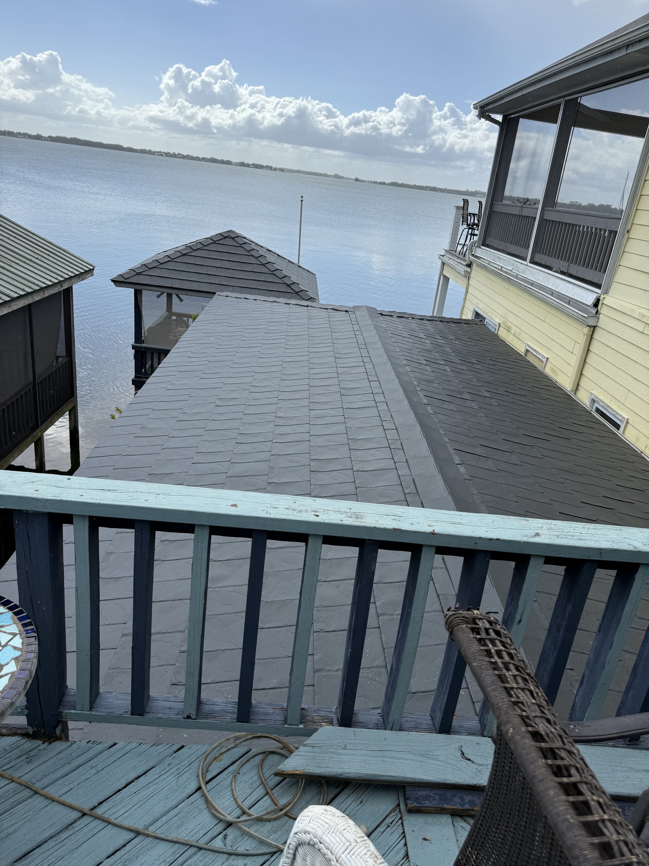 View from a balcony overlooking a calm lake with houses on stilts, partly cloudy sky, and distant forested shoreline.