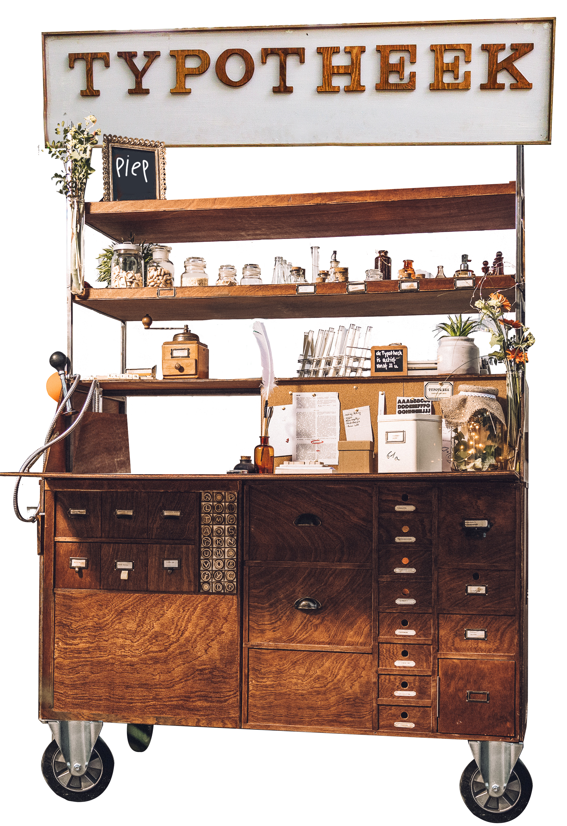 Een vintage apothekerskast met meerdere lades en houten planken, gevuld met kleine dozen, potjes en decoraties, met een bord met de tekst 'TYPO THEEK' bovenaan.
