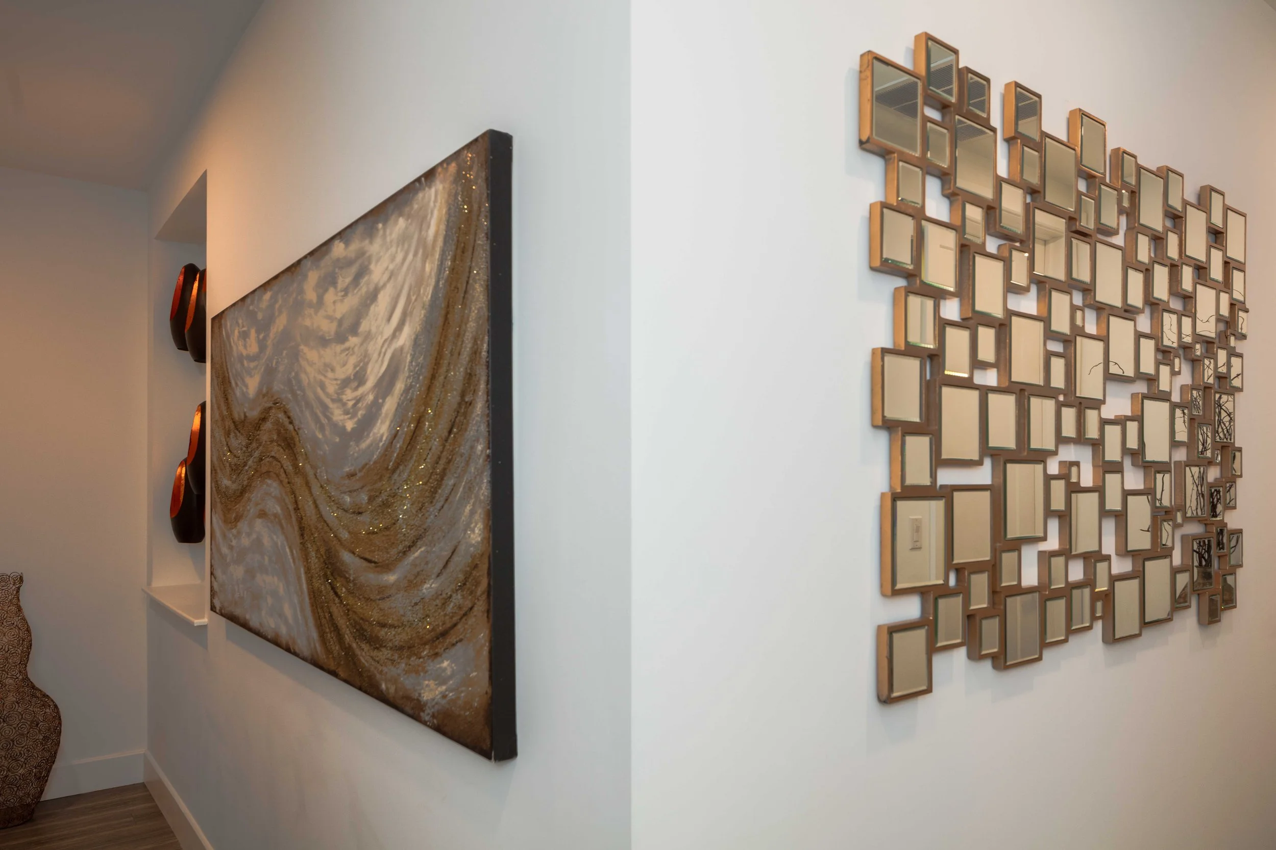 Side perspective of a large abstract swirl painting with gold and cream tones, adding movement and texture to a minimalist hallway.