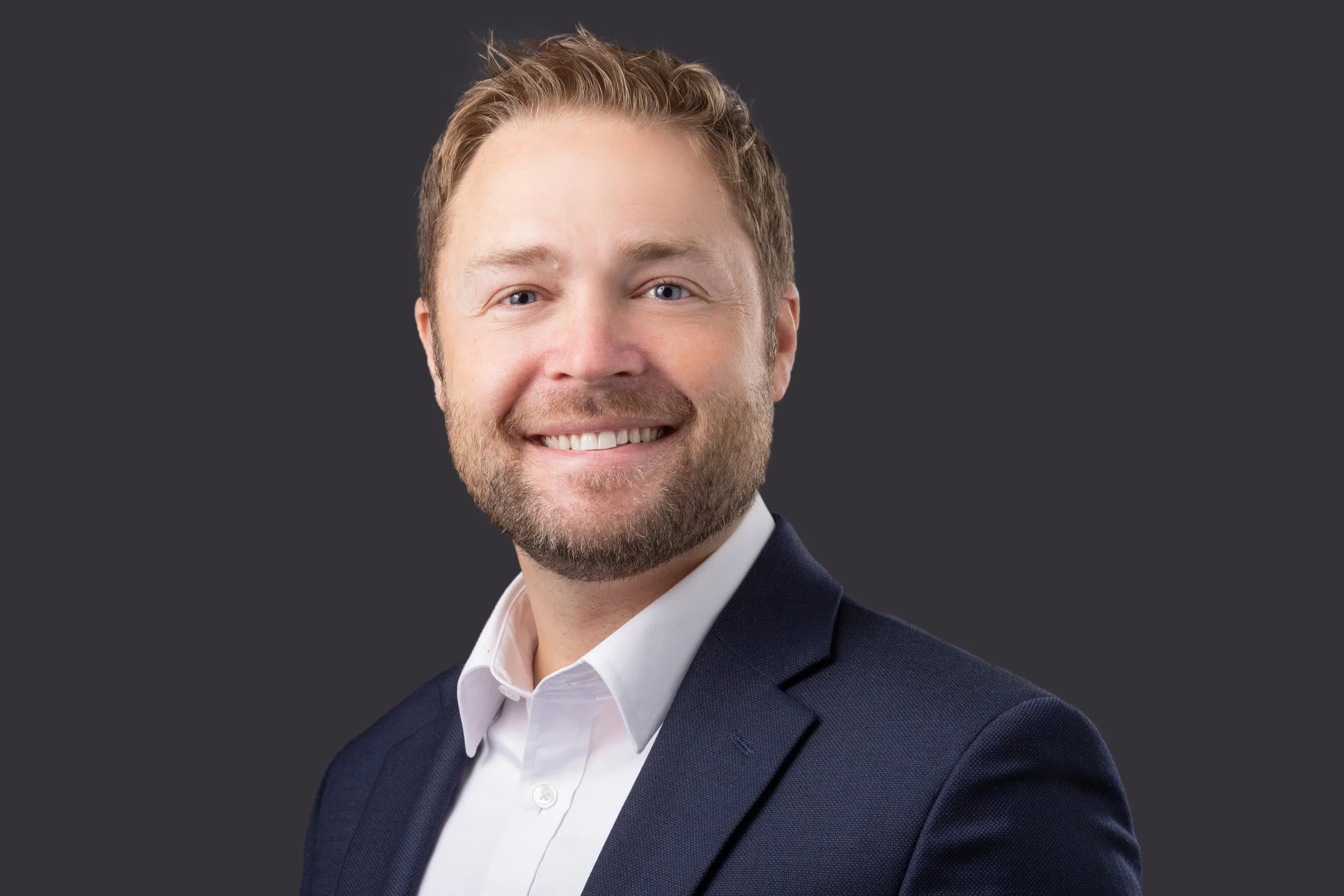 Smiling man in a suit with a dark background.
