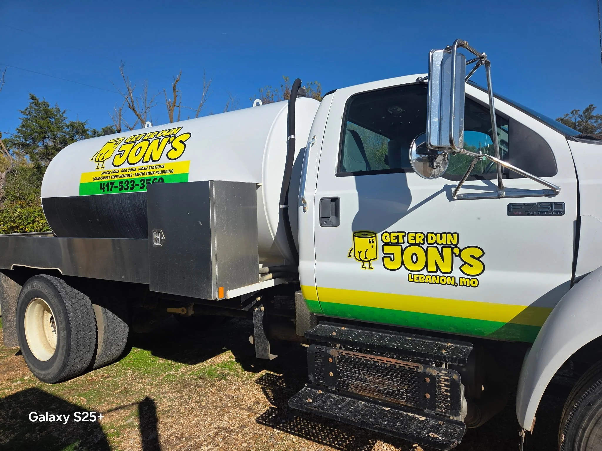 A white service truck with branding for Jon's, a plumbing company, parked outdoors under a clear blue sky. The truck has a large water tank on the back and logos promoting services in Lebanon, MO, with the company's phone number.