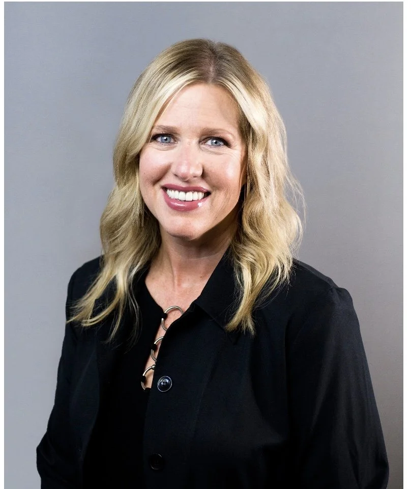 Smiling woman with blonde hair and a black jacket, portrait style.