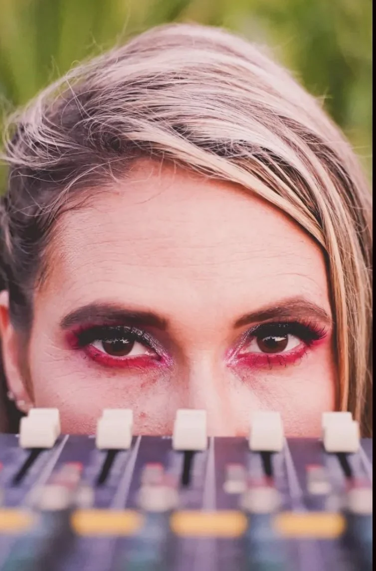 Close-up of a woman's eyes over a sound mixer with colorful eye makeup.