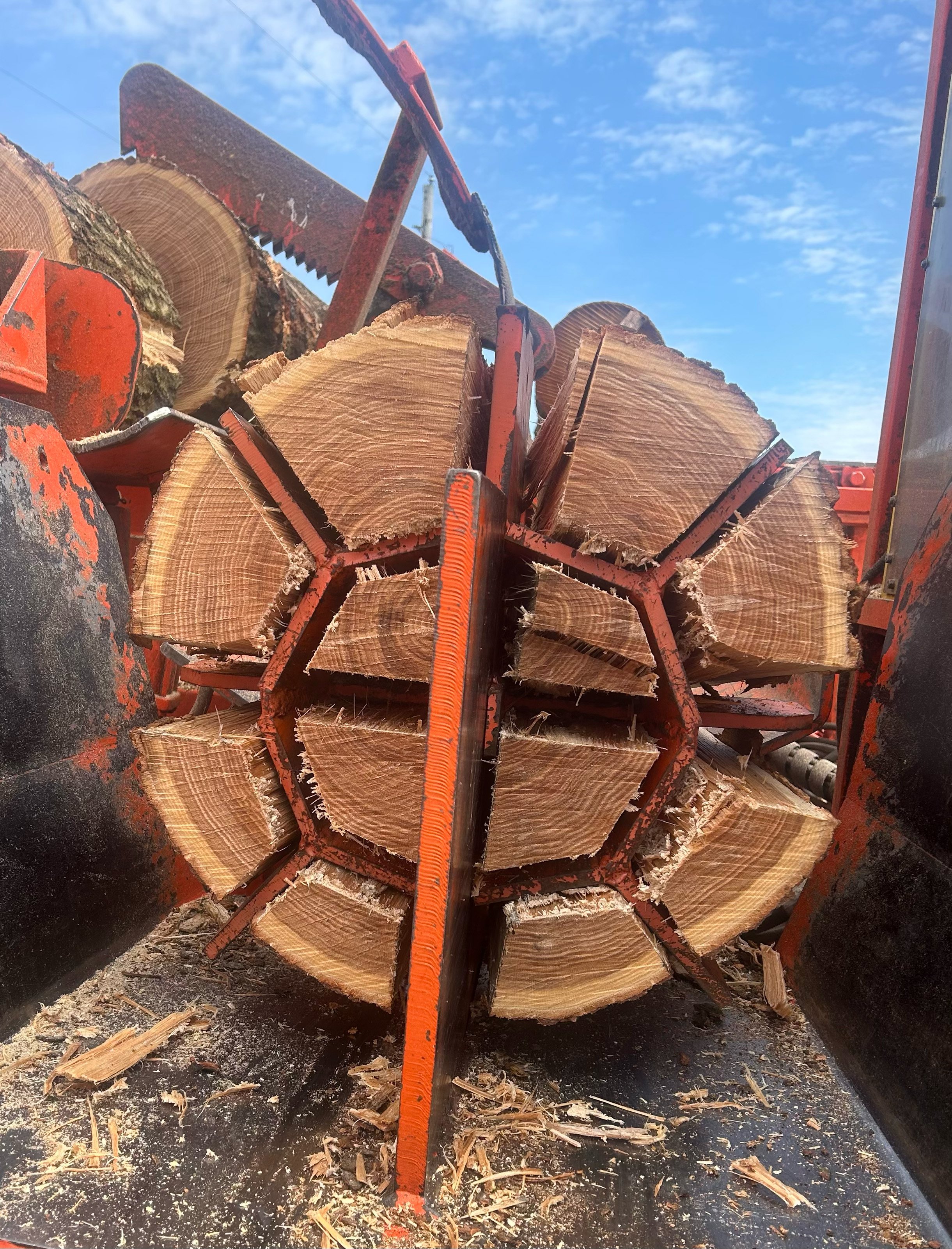 A machine cutting a large log into sections for firewood under a blue sky.