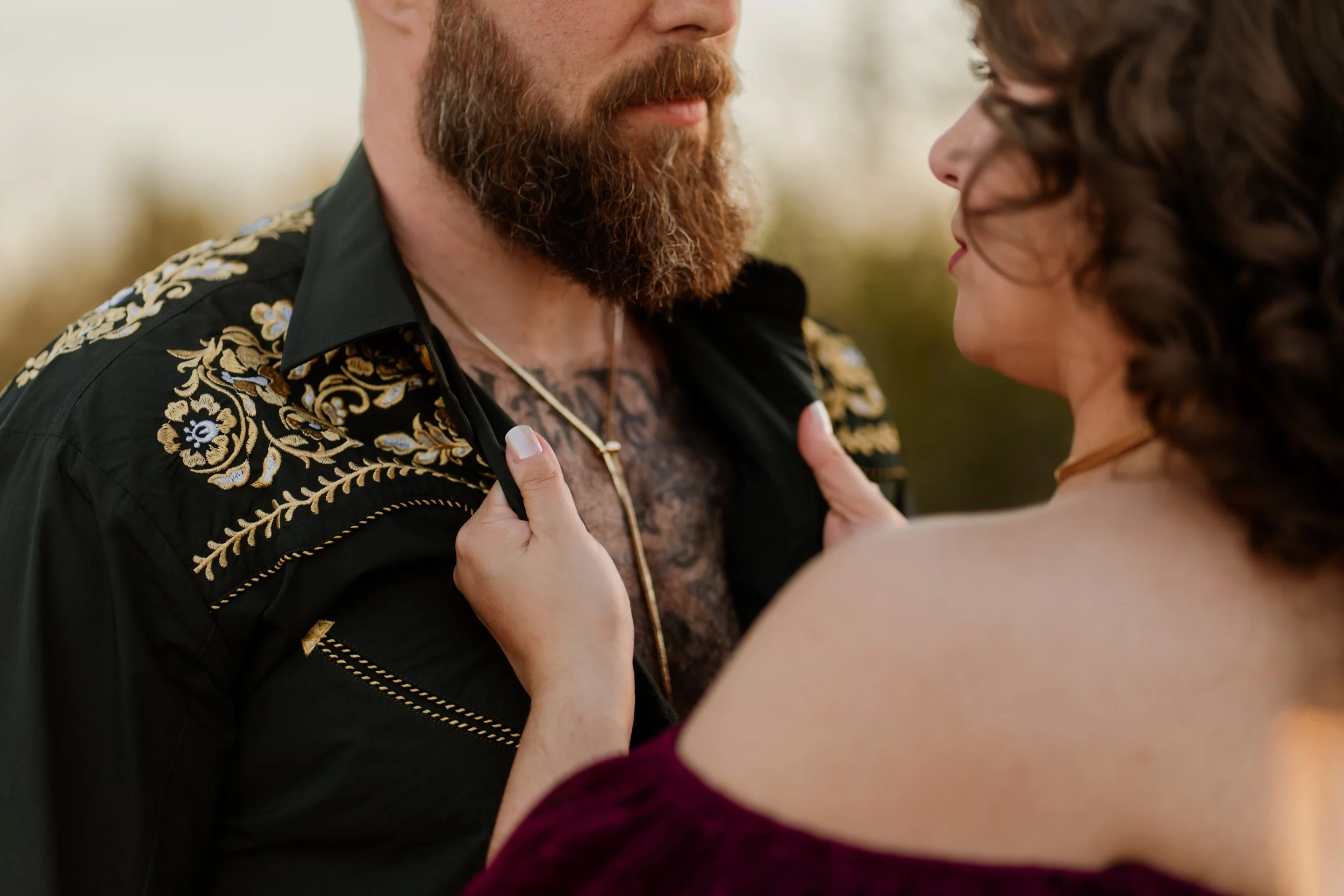 A woman grabs the collar of a man's green embroidered western style shirt for a couples photoshoot.