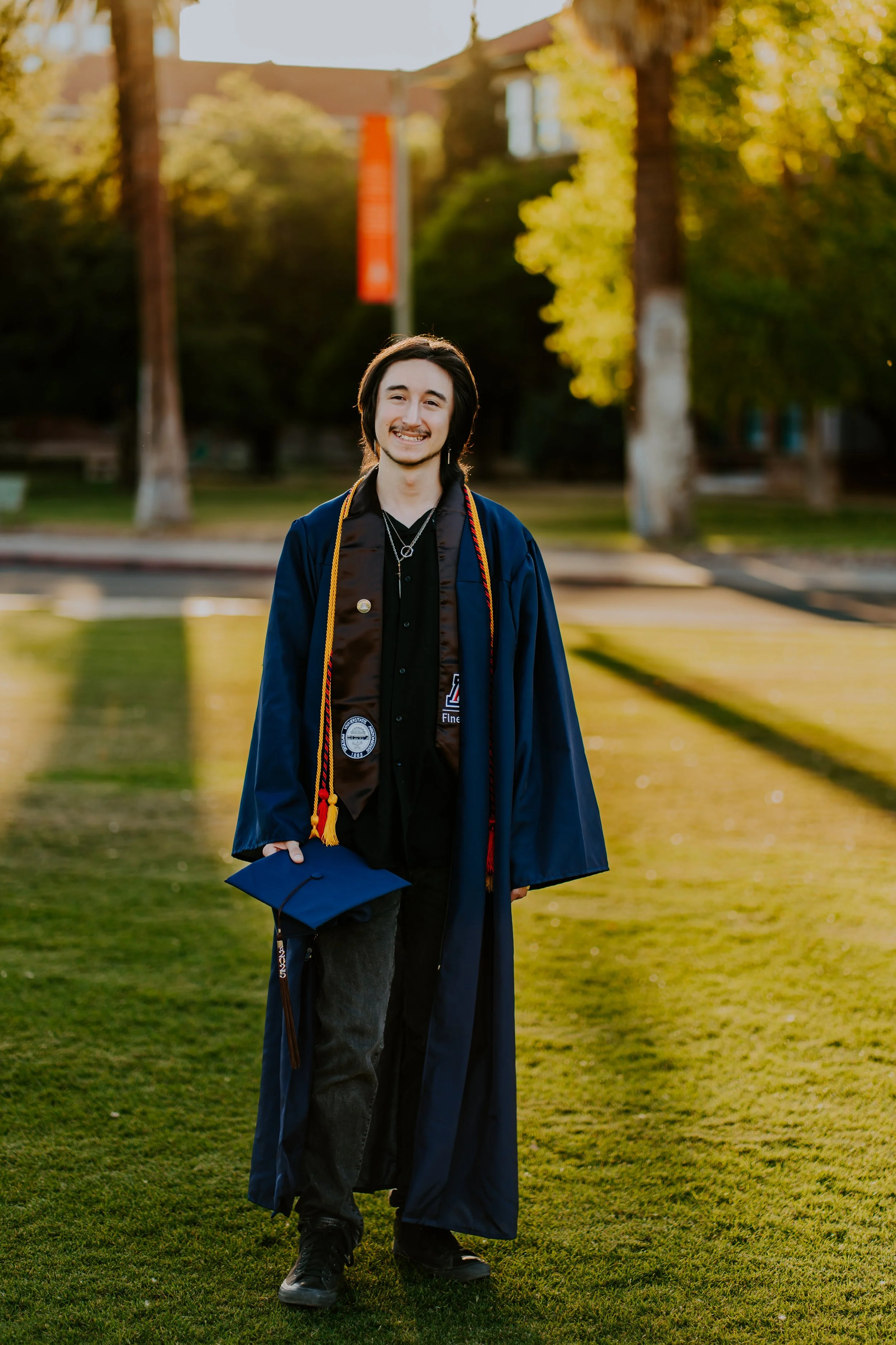 A man who is graduating college poses for a senior grad photoshoot during sunset on the University of Arizona lawn.