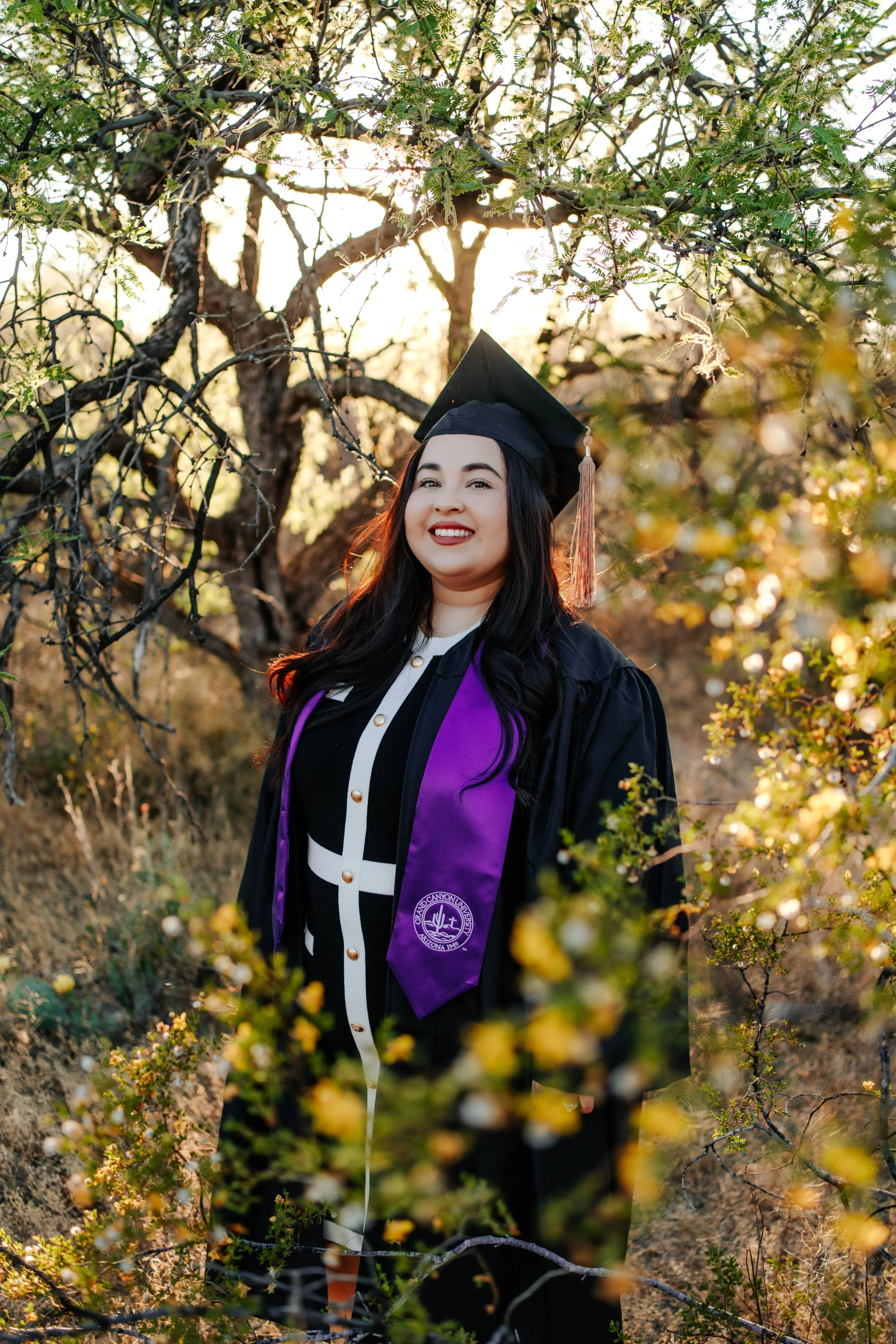 A woman stands in the Sonoran desert in Tucson, Arizona smiling at the camera for her graduation photoshoot.