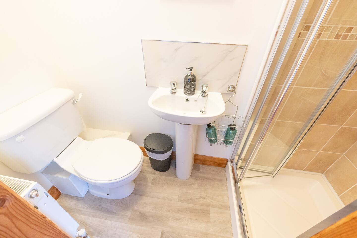 Small bathroom with toilet, pedestal sink, shower enclosure, and waste bin