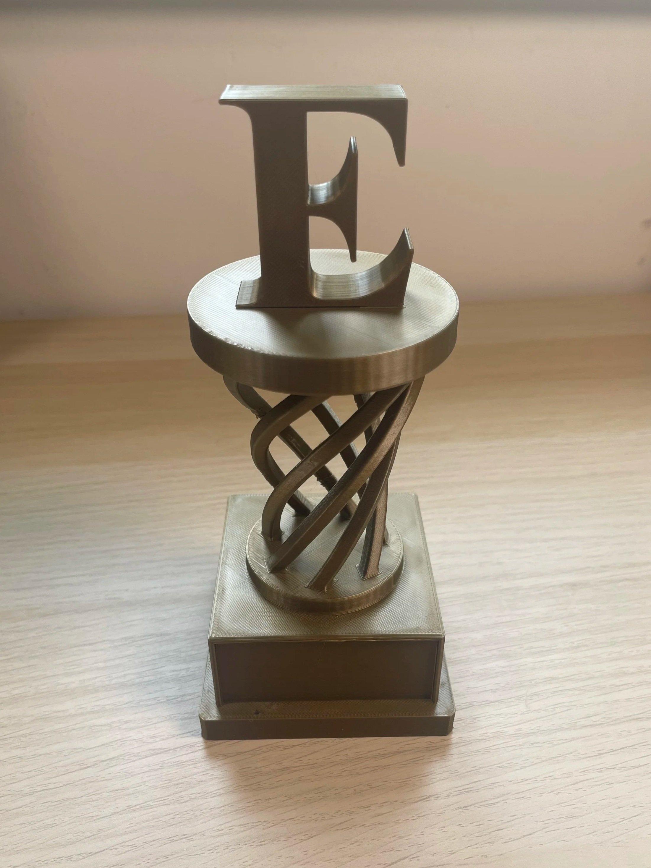 A silver decorative sculpture featuring the letter 'E' on top of a twisted, spiral base, mounted on a square platform.