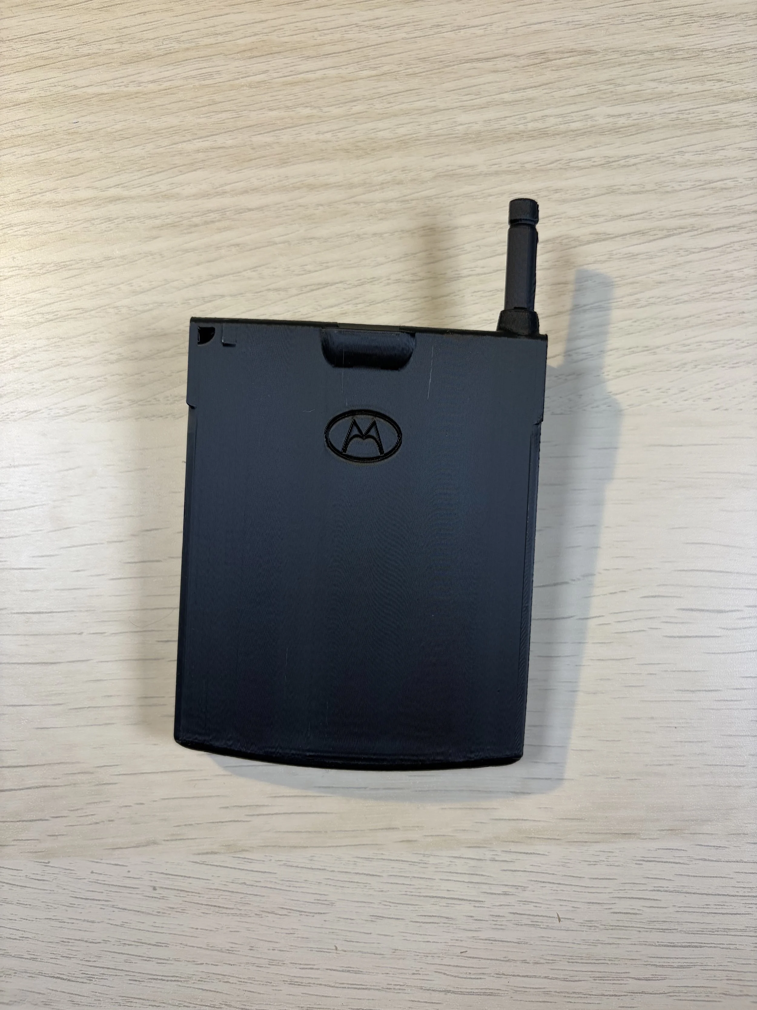 A Motorola flip phone with an antenna on a light-colored wooden surface.