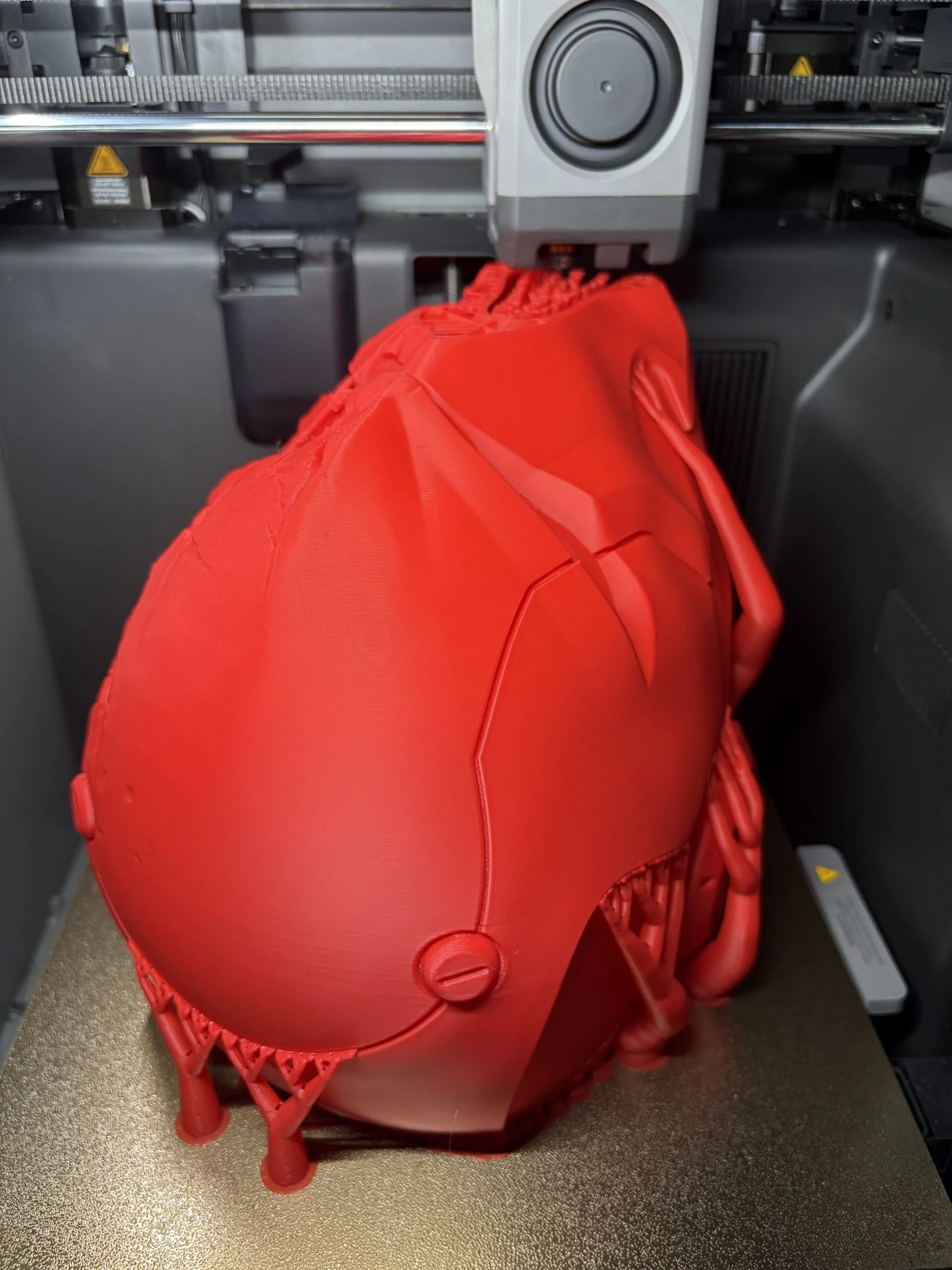 A red 3D printed object, possibly a spacecraft model, is being printed on a 3D printer.