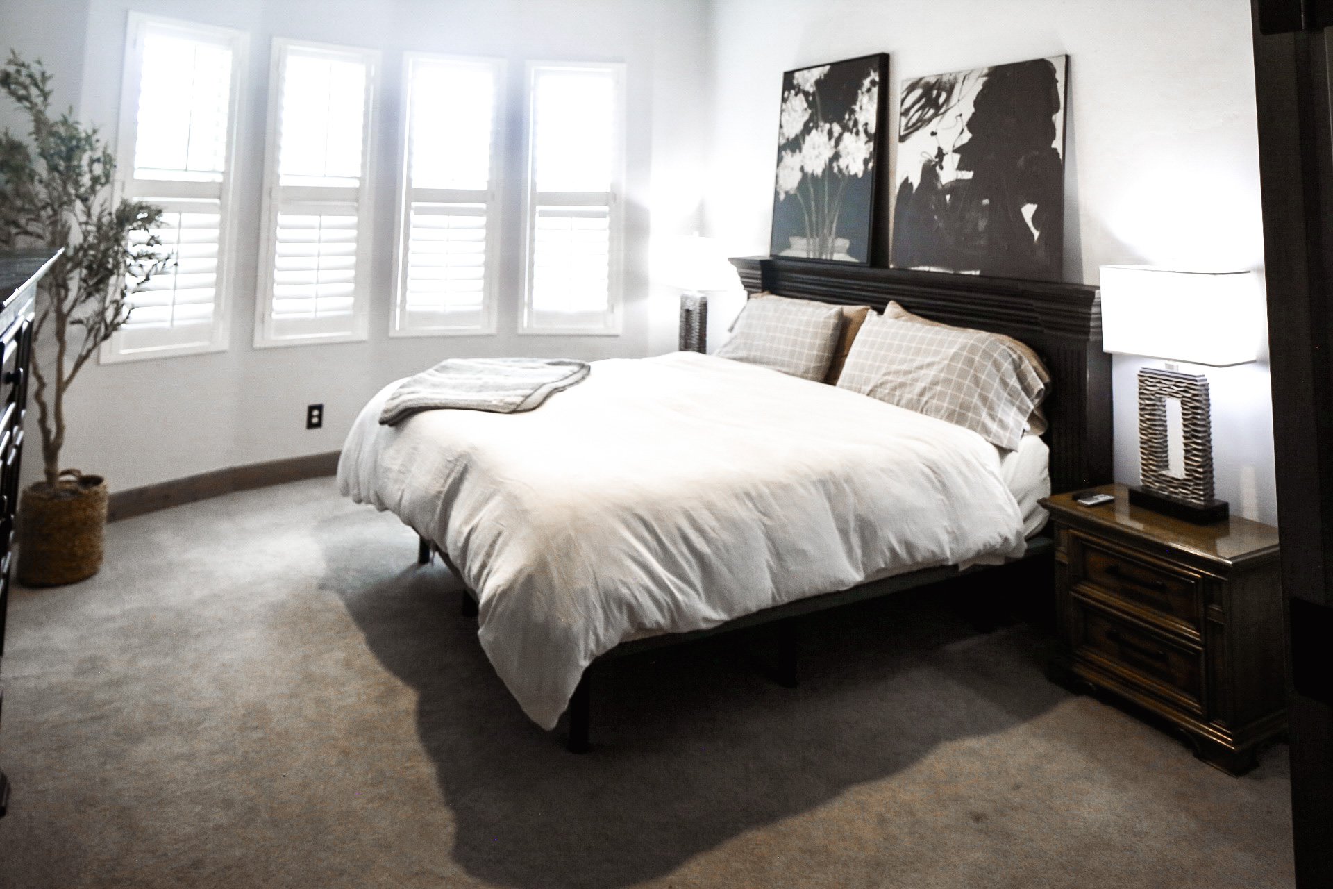 The Clubhouse Suite features a split-king adjustable bed, custom artwork, bedside table with USB charging lamps, and plantation shutter windows overlooking the golf course.