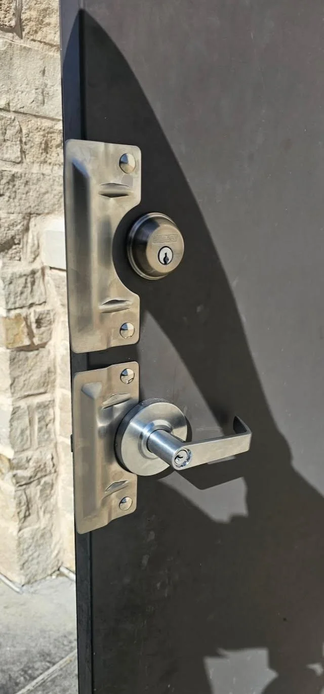 A close-up of a black door with a silver lock and handle, attached to a brick wall, casting a shadow.