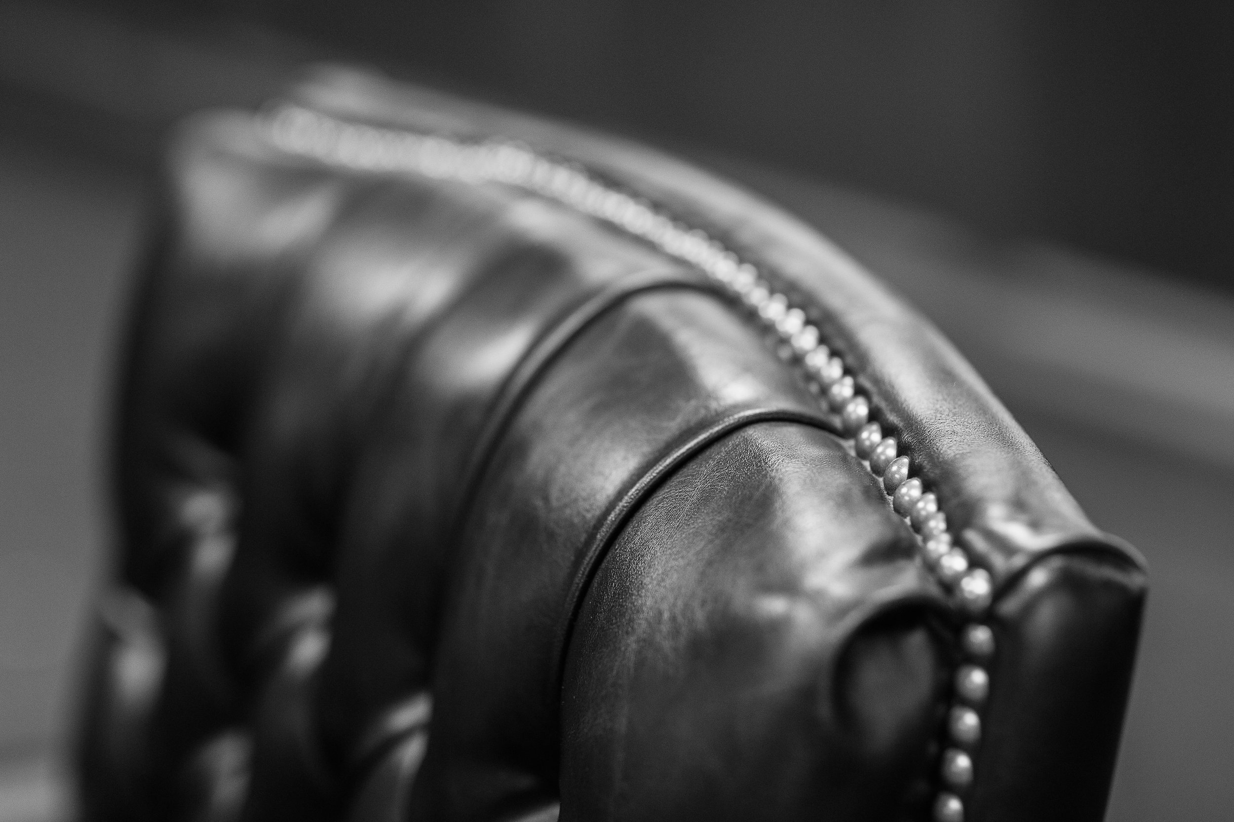 Close-up of a vintage leather armchair with decorative nailhead trim, black and white photograph.