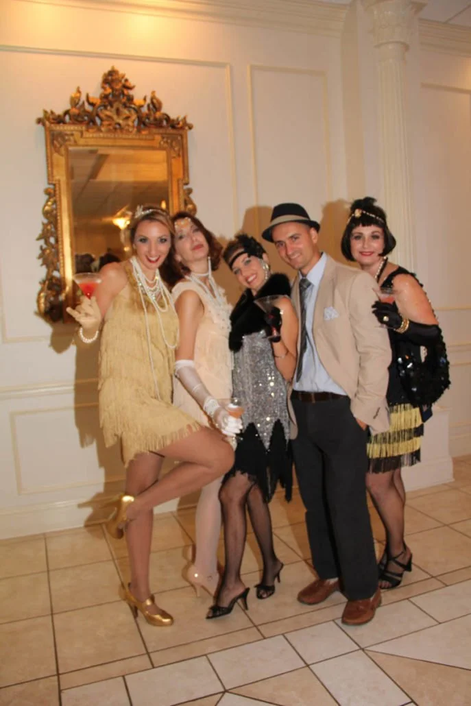 Group of five people dressed in 1920s flapper costumes and vintage accessories at a party.