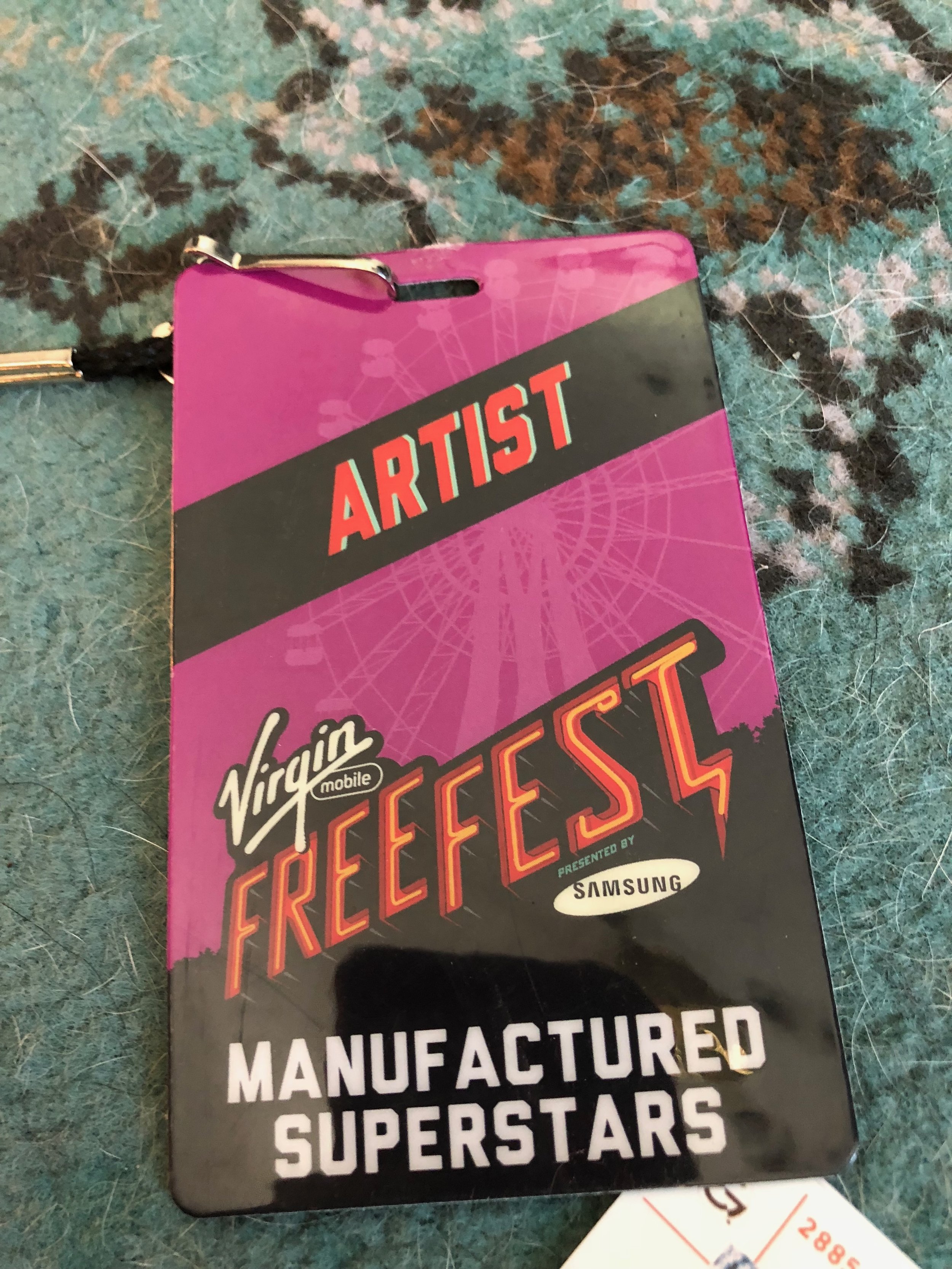 Festival badge for Virgin Mobile FreeFest, presented by Samsung, with the tagline 'Manufactured Superstars', showing a purple and black background with a ferris wheel outline.
