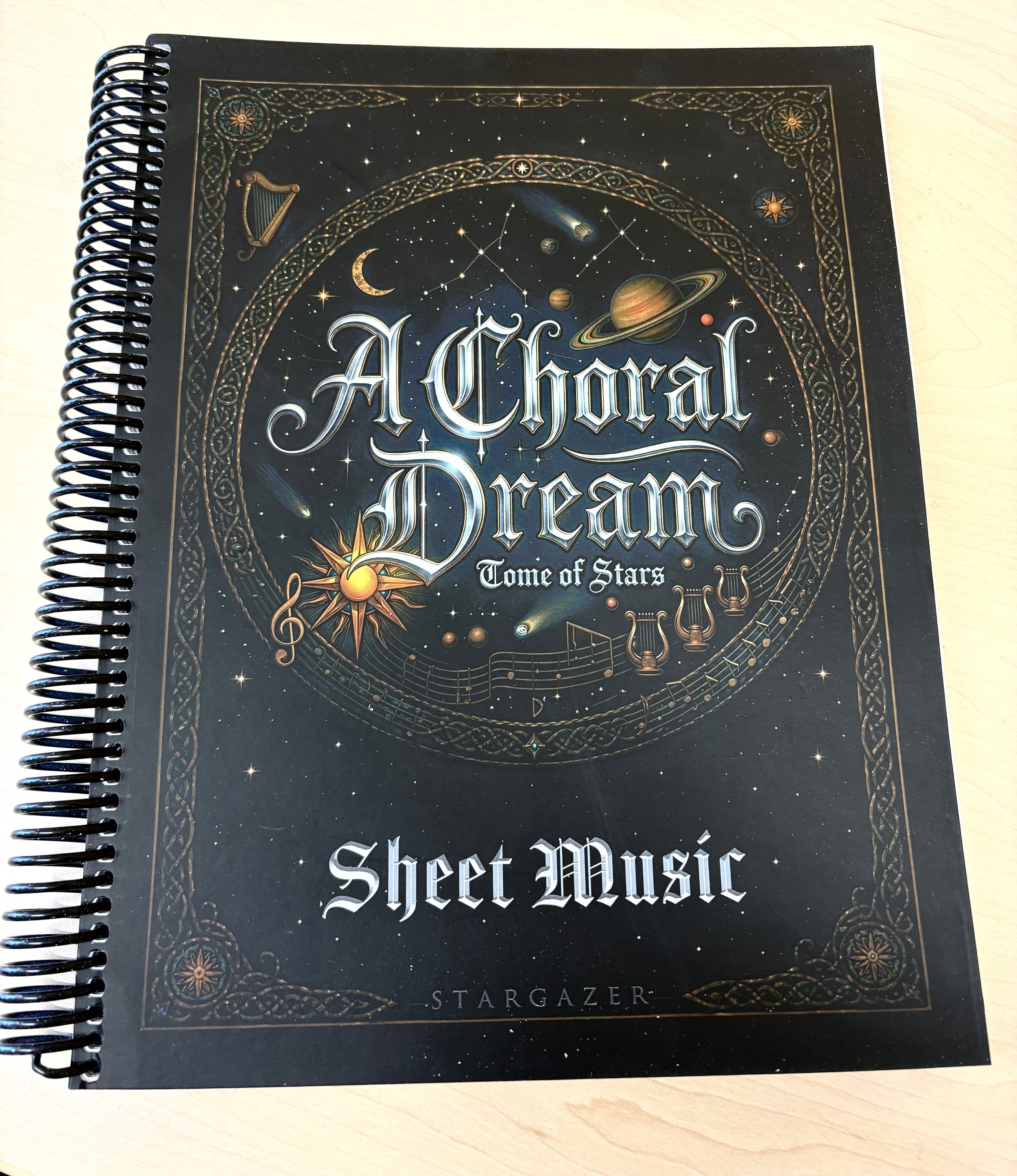 Photo of the choral sheet music anthology "A Choral Dream" showing the spiral bound collection with the celestially illustrated cover