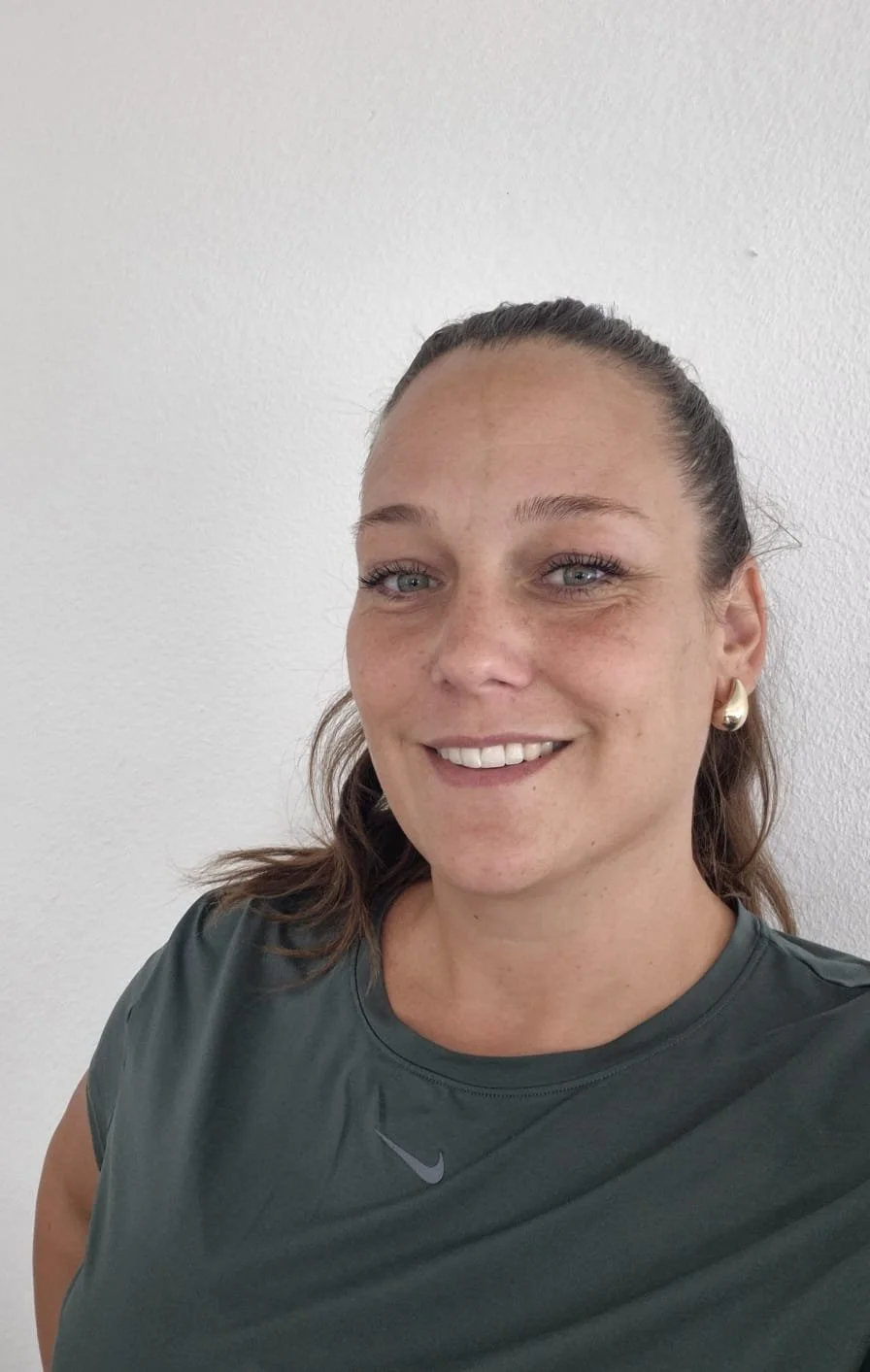 Une femme souriante portant un haut gris avec le logo Nike, earrings en forme de boucle, face à un mur blanc