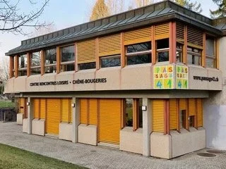Bâtiment commercial avec volets de magasins jaunes, fenêtres avec lamelles en bois, panneau de signalisation vert, jaune, rouge et bleu, et une boutique de confiseries.