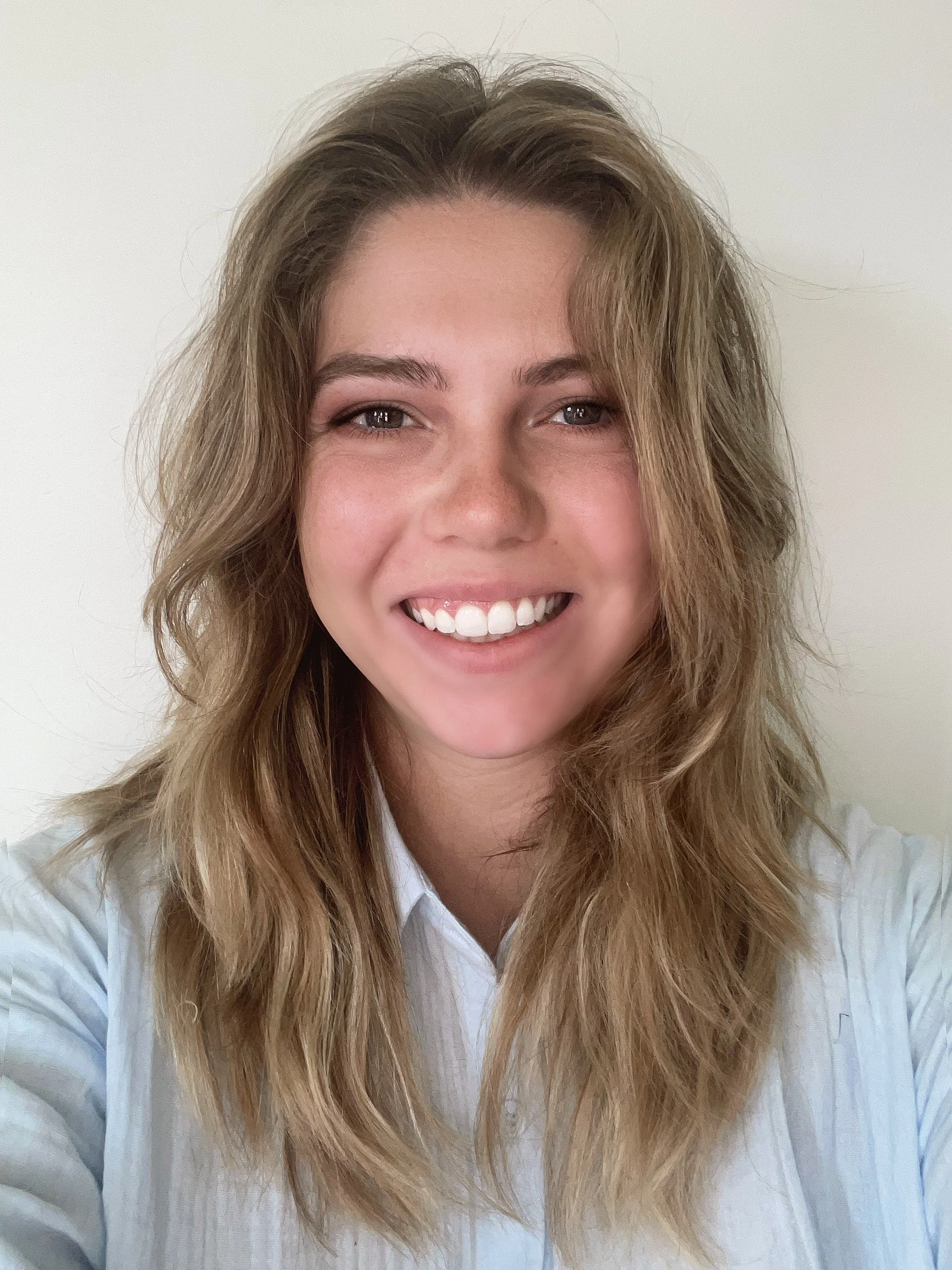 blonde white woman wearing a blue shirt smiling at the camera