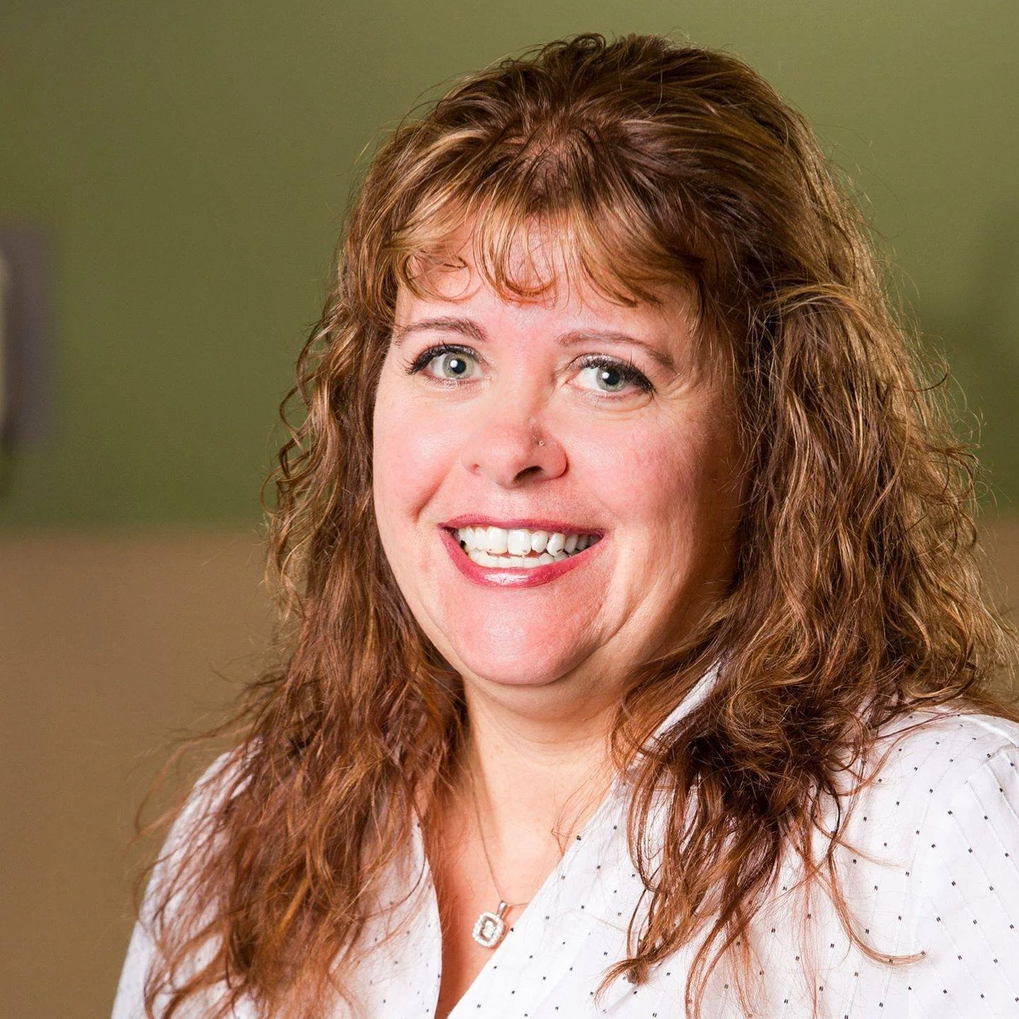 Smiling woman with curly brown hair and a light-colored shirt.