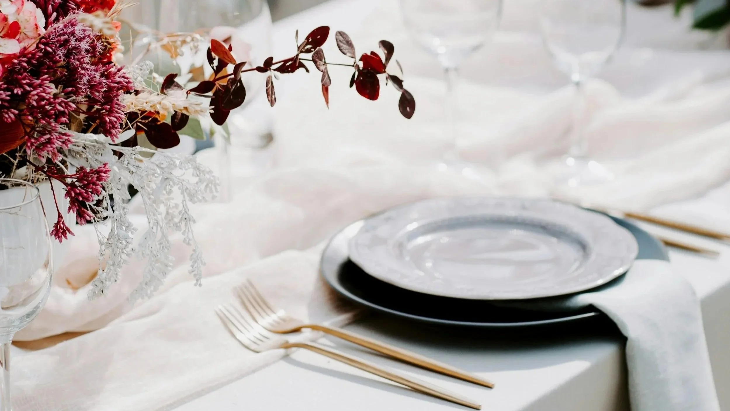 Elegant table setting with a floral centerpiece, stacked plates, and gold utensils on a white tablecloth.