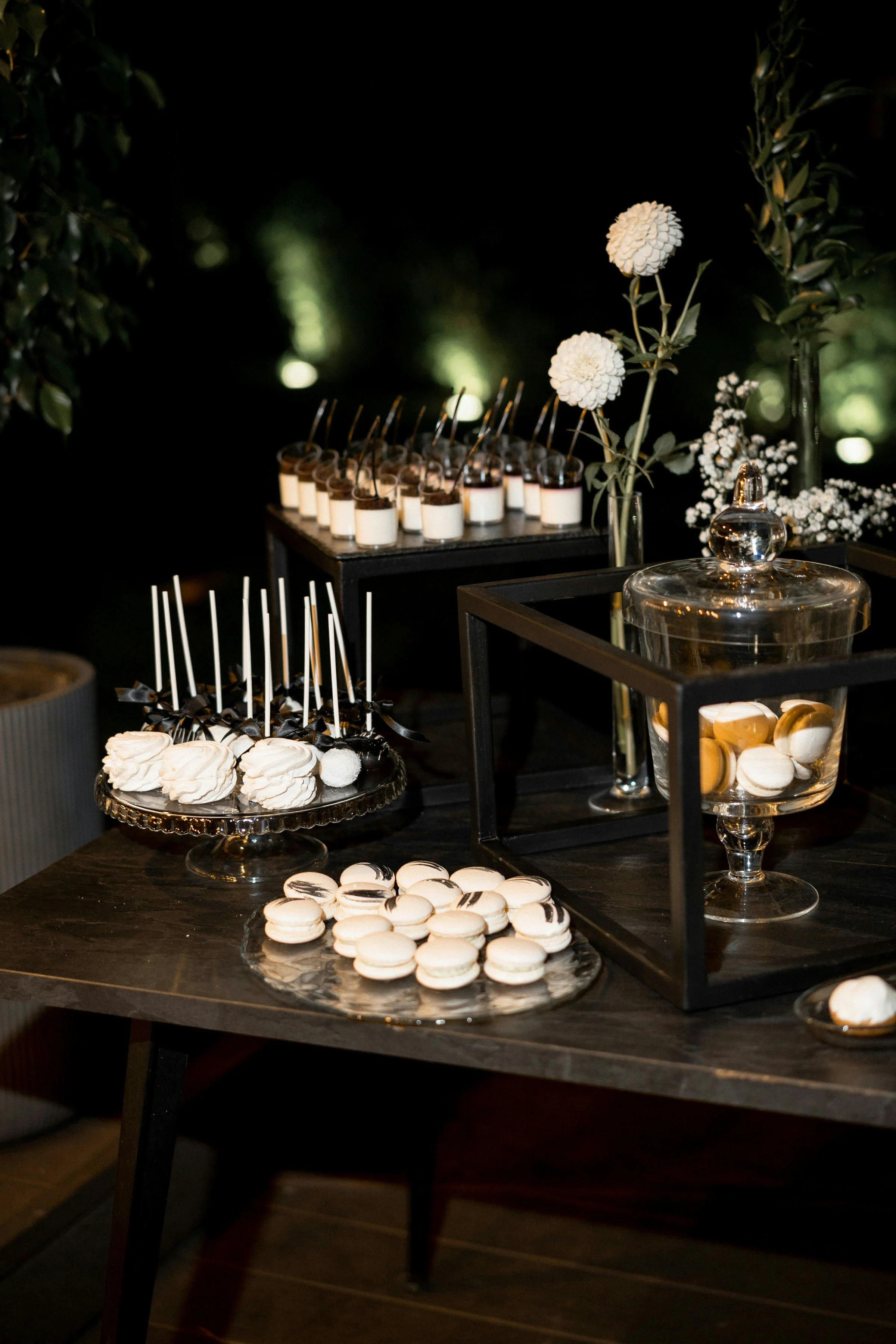 Dessert table with macarons, meringues, and chocolate treats, decorated with white flowers, at a corporate event.