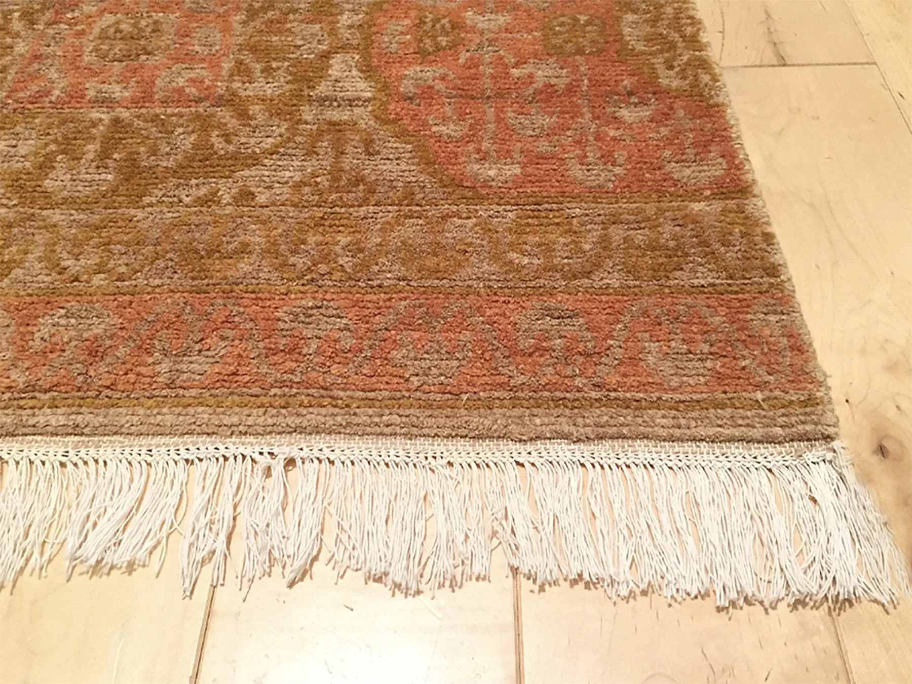 Close-up of a traditional patterned area rug with fringed edge on a wooden floor.