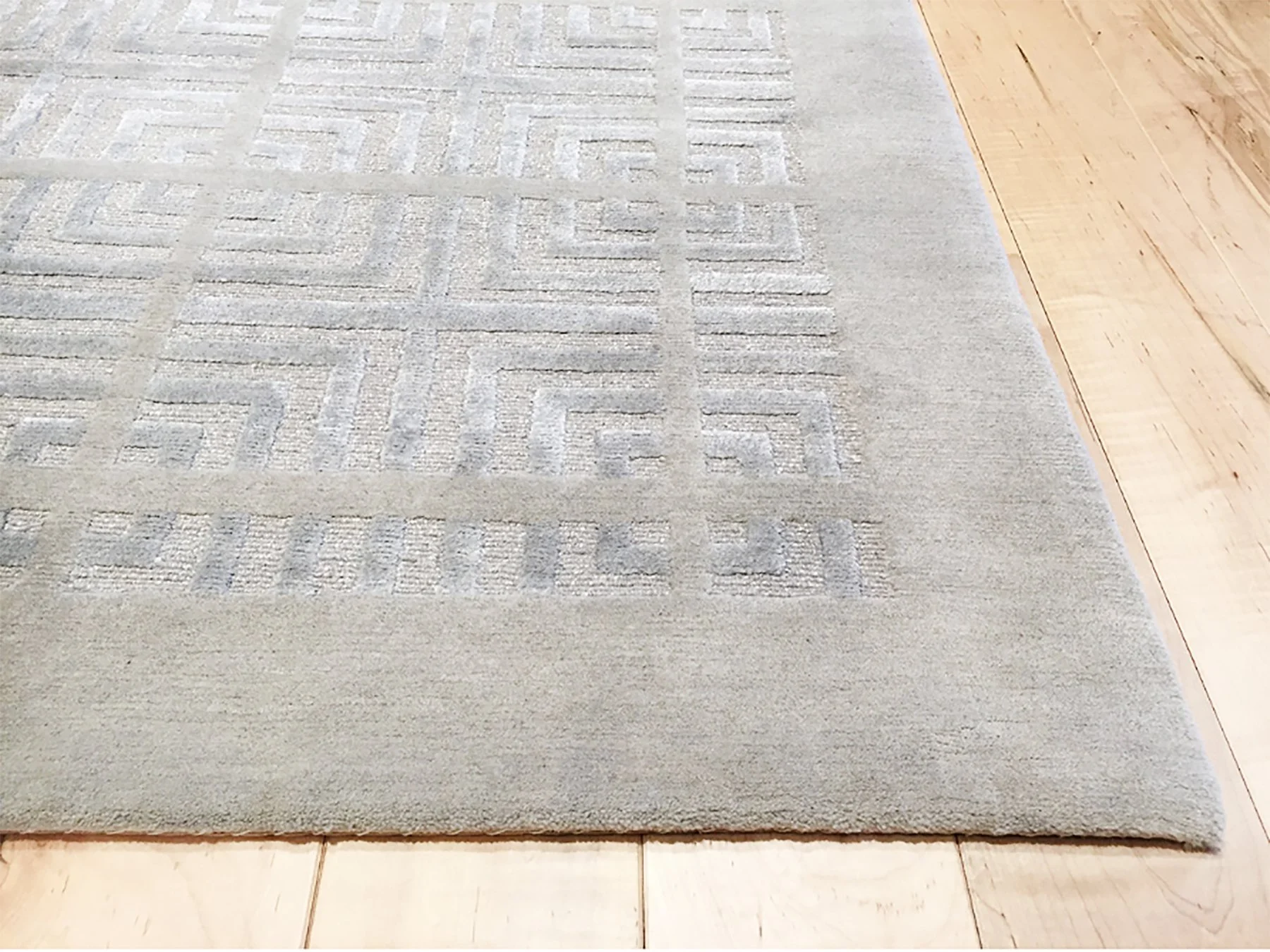 Close-up of a light-colored textured area rug with a plain border, situated on a hardwood floor.