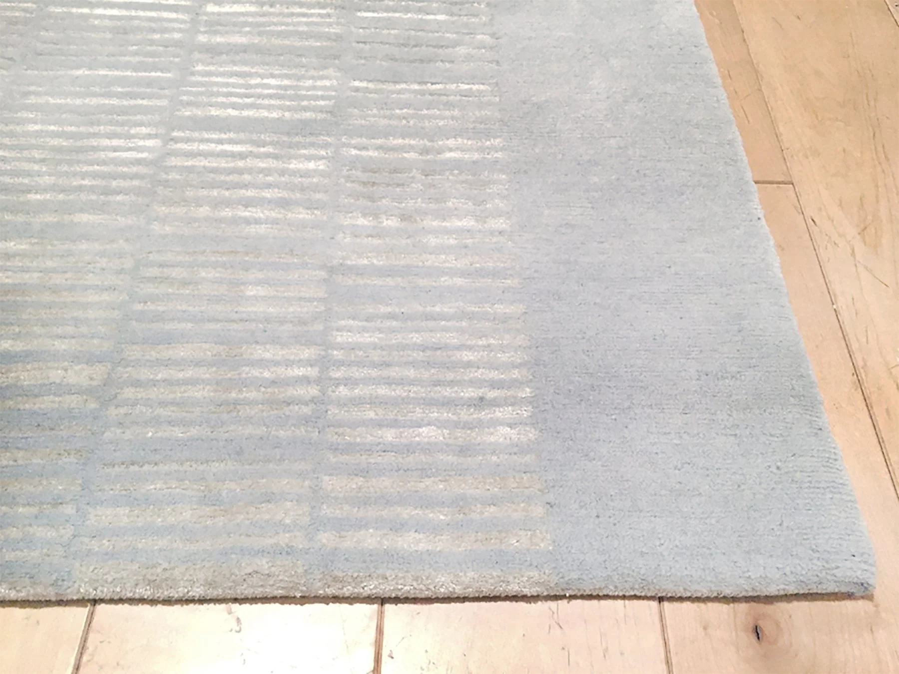 Close-up of a pale blue rug with textured vertical and horizontal lines, laid on a wooden floor.