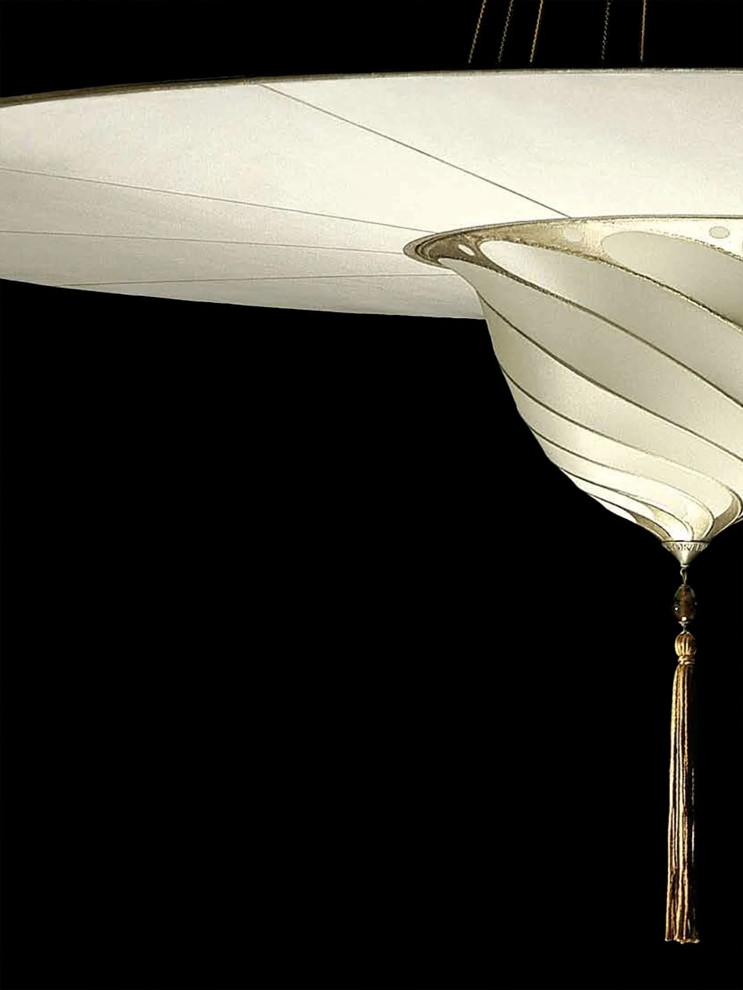 Close-up of a vintage hanging lamp with a white silk shade and a decorative tassel at the bottom against a black background.