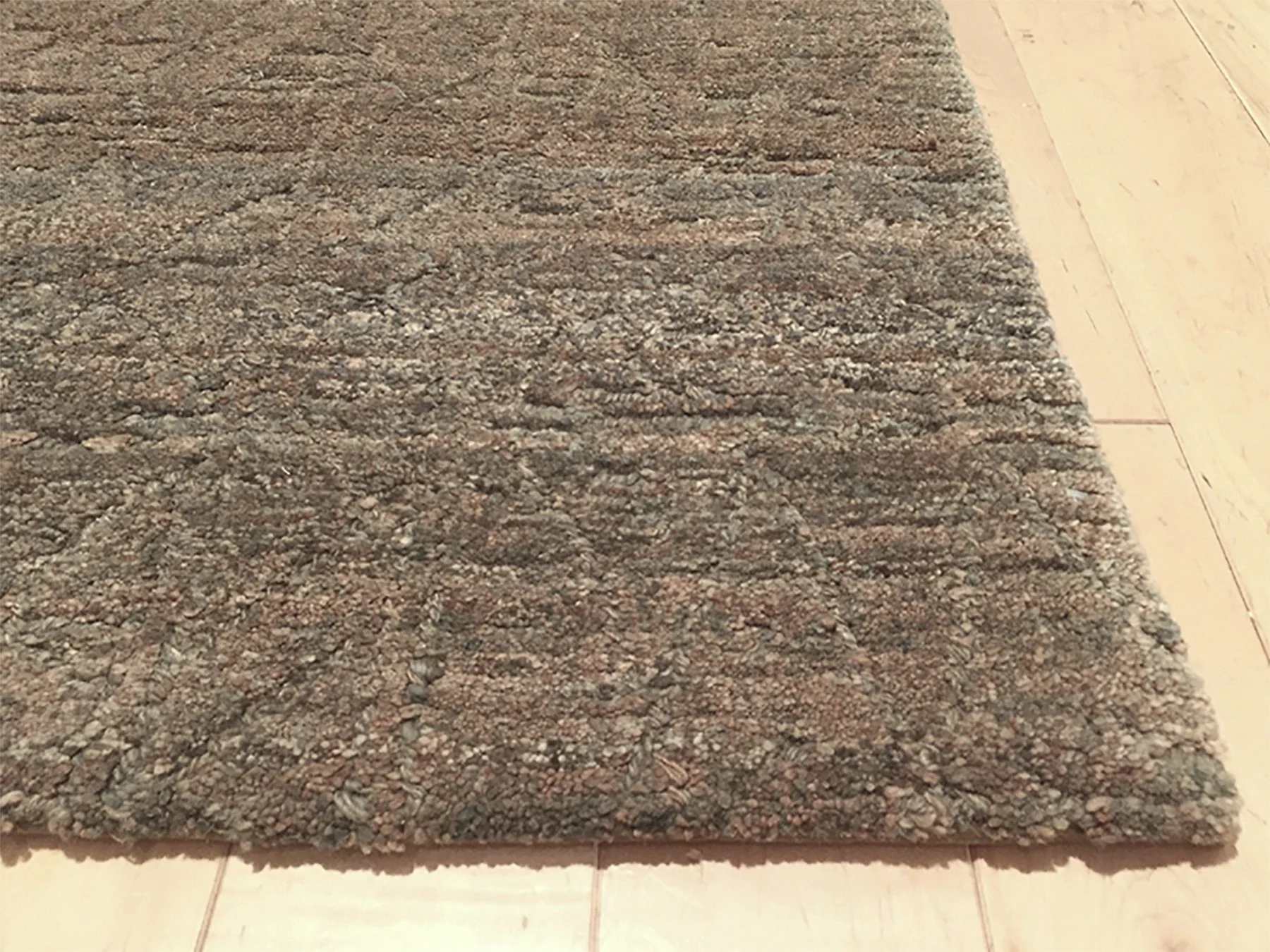 Close-up of a textured, multicolored area rug on a light wood floor.