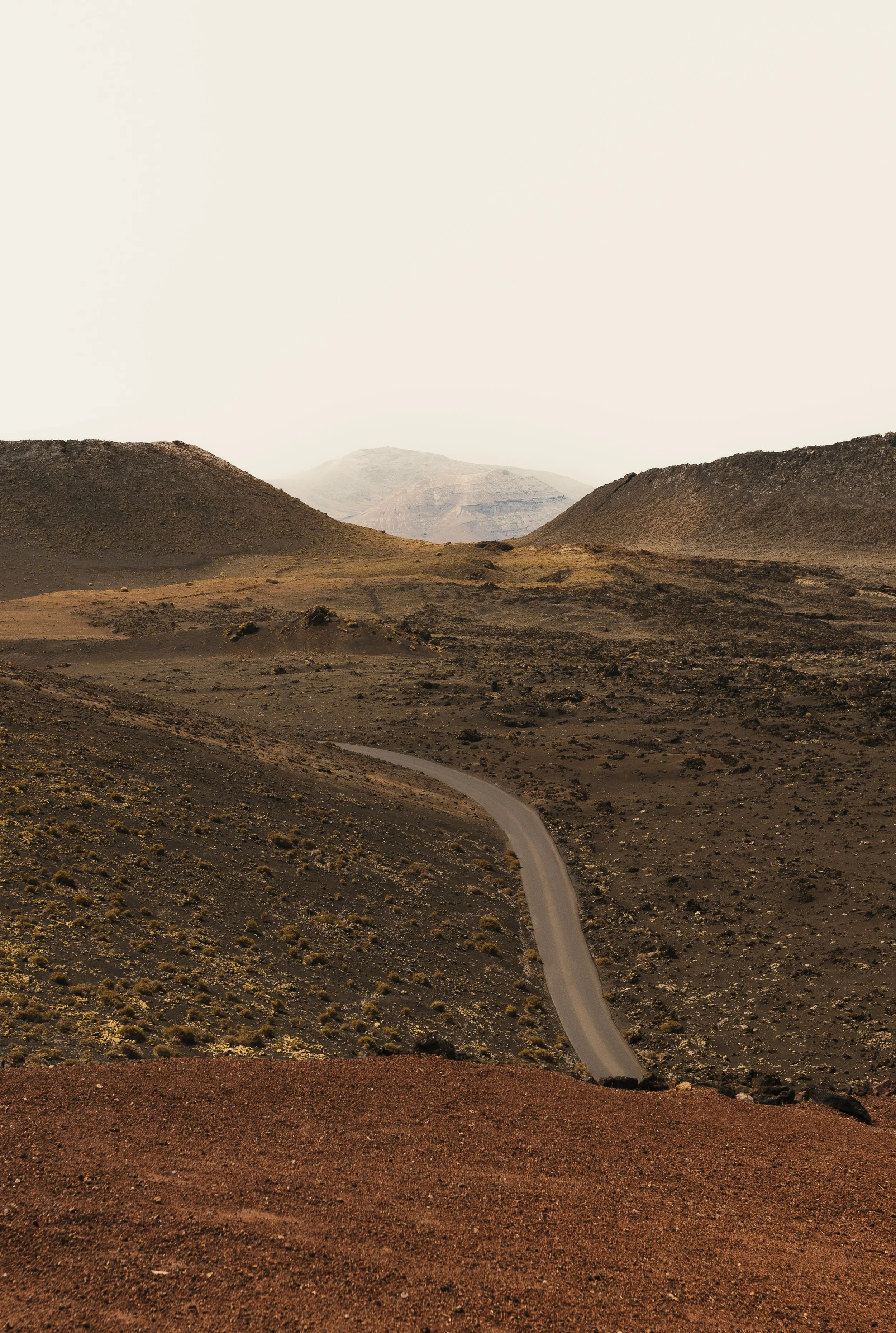 Paesaggio desertico con una strada tortuosa che attraversa colline rocciose e montagne lontane.