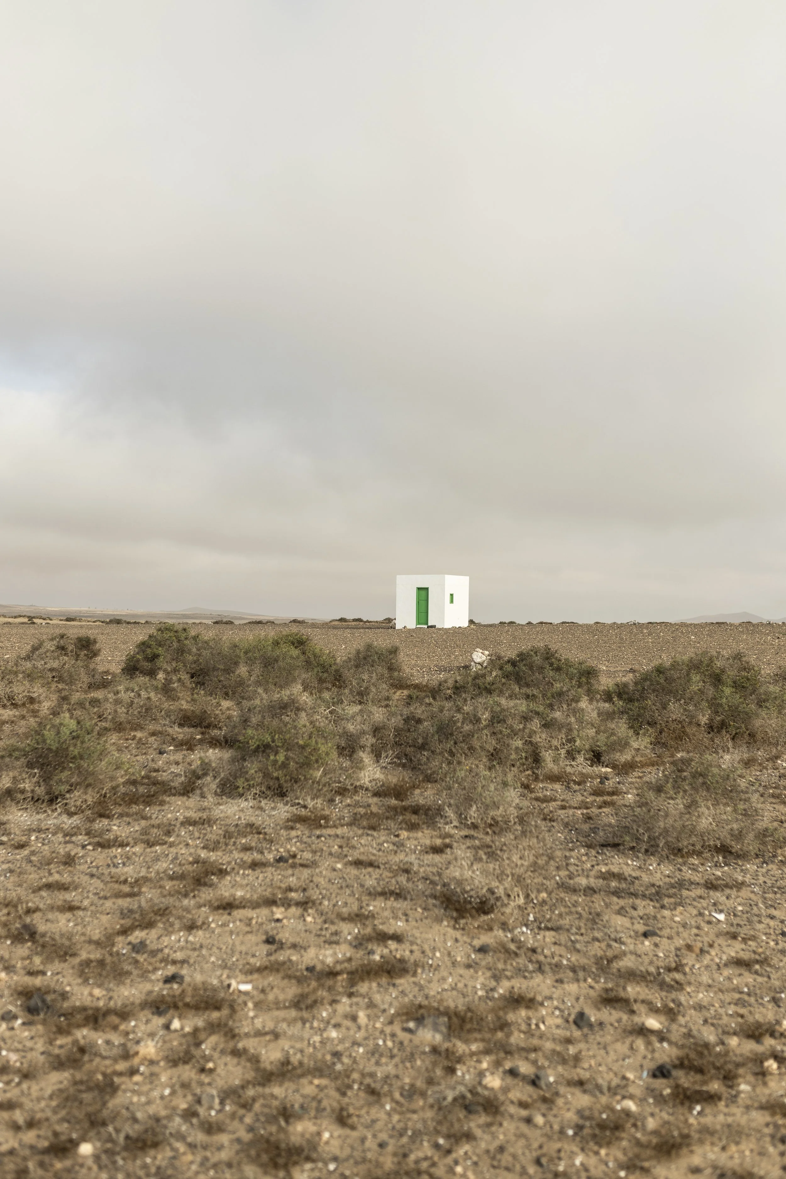 Casa bianca piccola con porta e finestra verdi in un paesaggio desertico con cielo nuvoloso