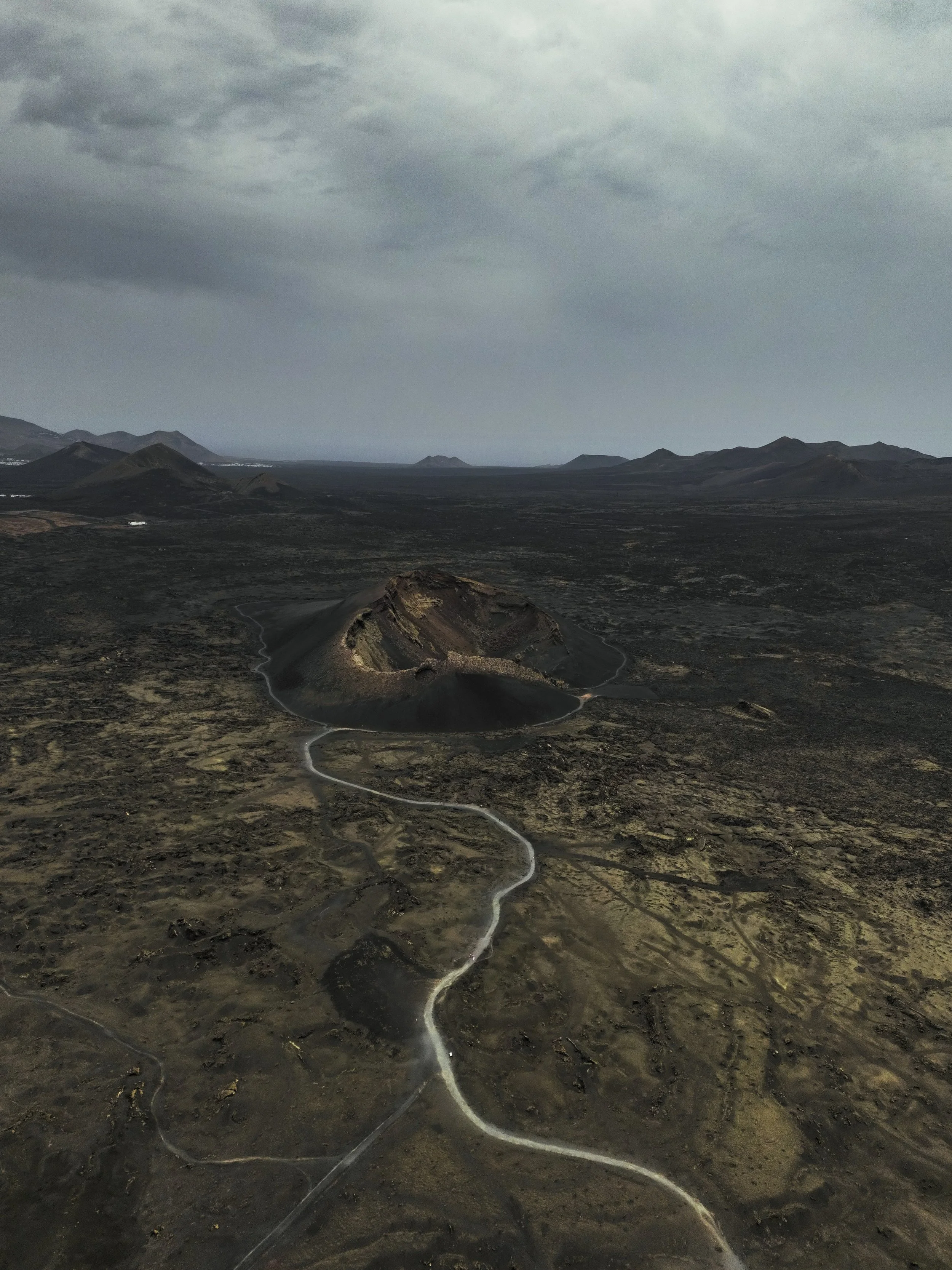Paesaggio vulcanico con un vulcano attivo al centro e strade che lo circondano, sotto un cielo nuvoloso.
