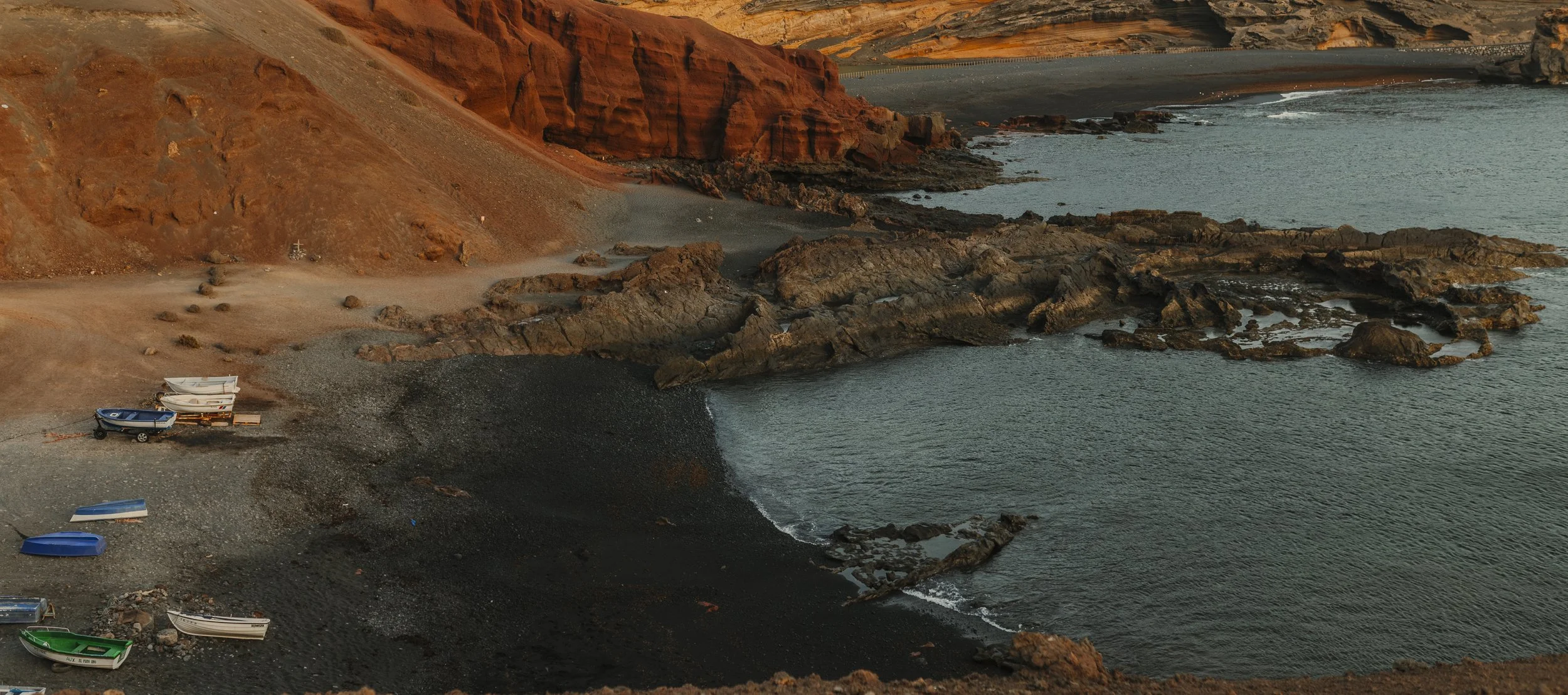 Spiaggia con barche rovesciate e rocce nere sulla costa, con scogli e acque calme.