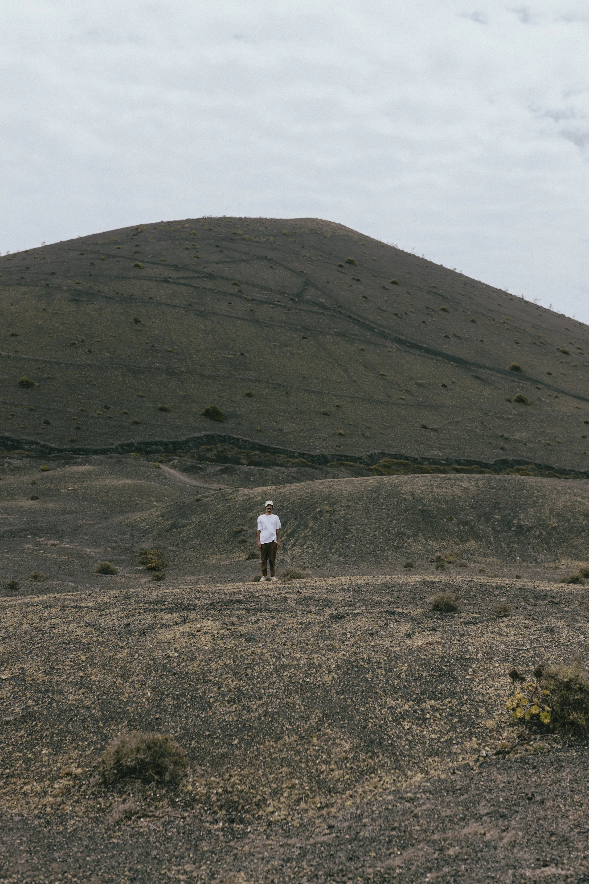 Uomo che cammina in un paesaggio desertico con una grande collina sullo sfondo sotto un cielo nuvoloso.