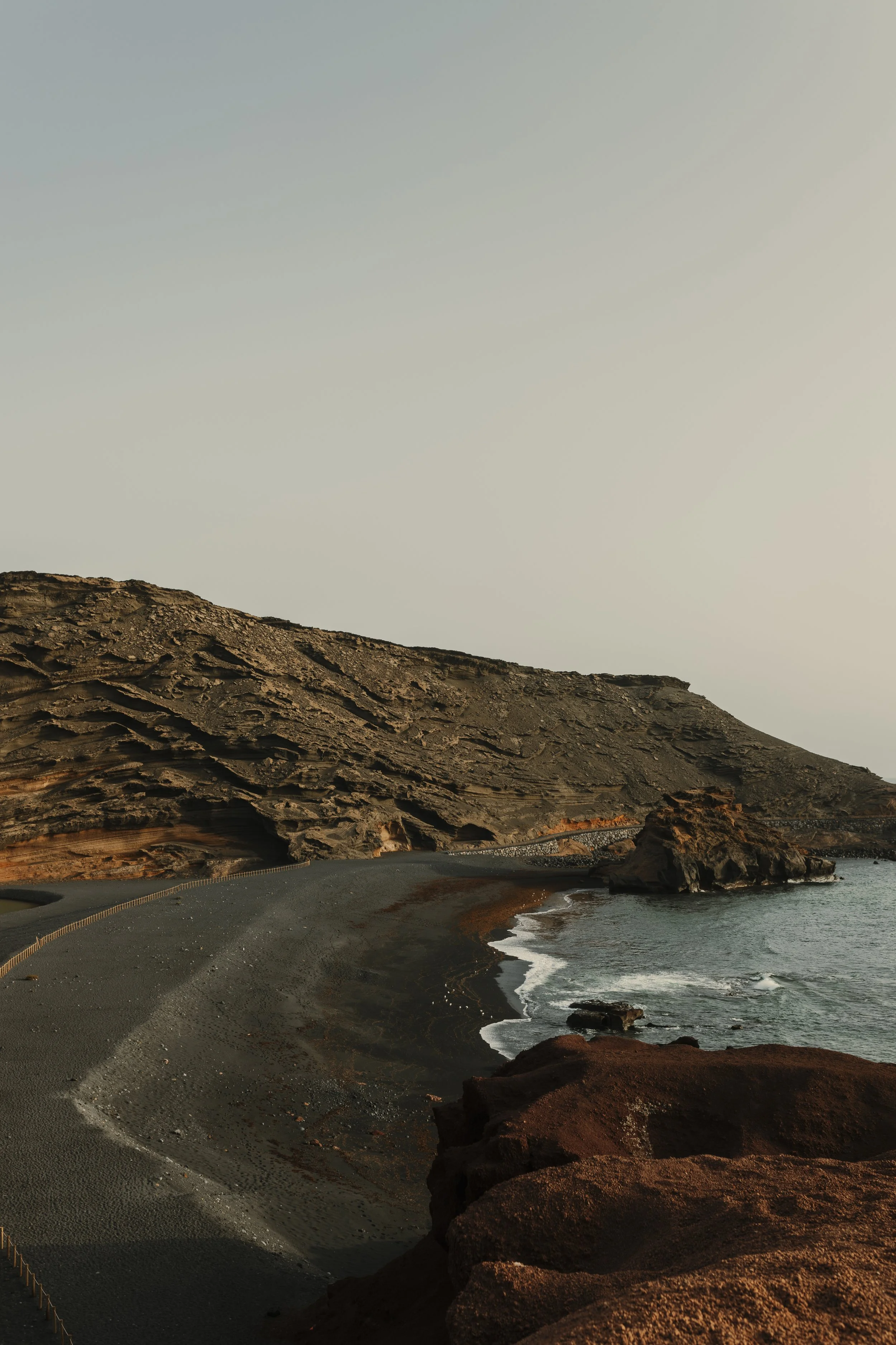Costa vulcanica con scogli e mare, sotto un cielo chiaro, al tramonto.
