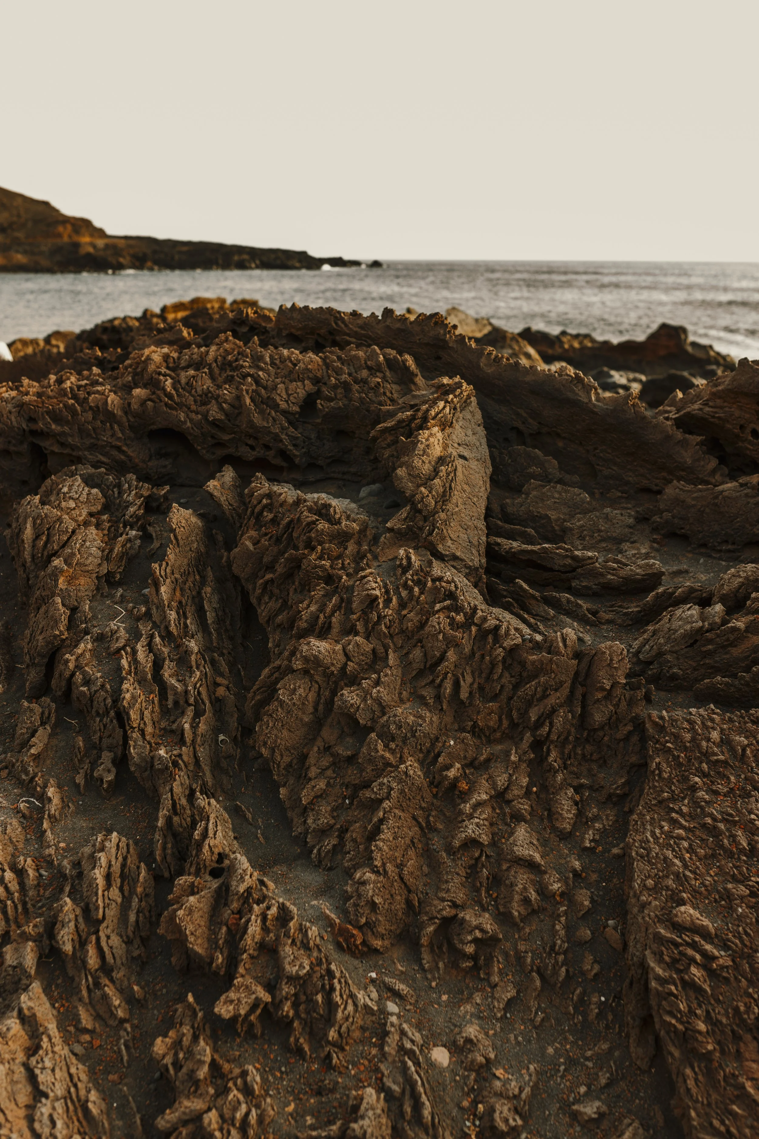 Scorcio di rocce sulla spiaggia con il mare sullo sfondo durante il tramonto.