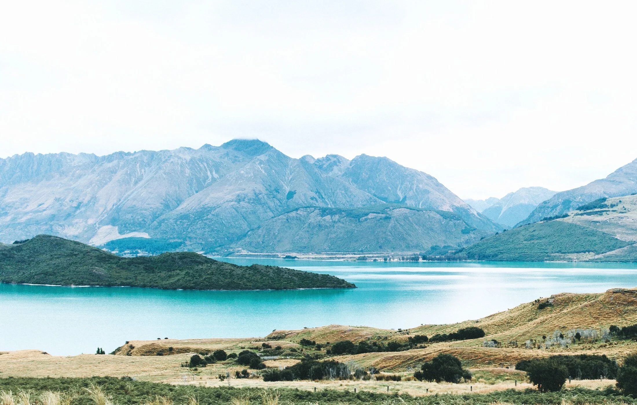Scenic landscape with mountains and lake, grassy hills in foreground.