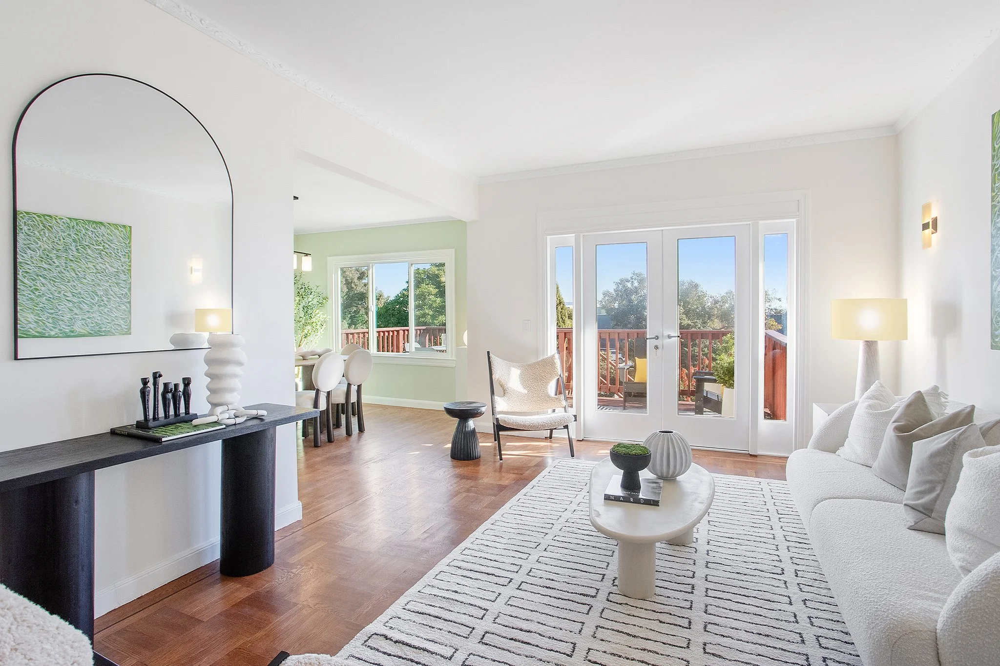 Bright living room with white couch, modern coffee table, and sliding glass doors leading to a balcony, with a view of trees outside.