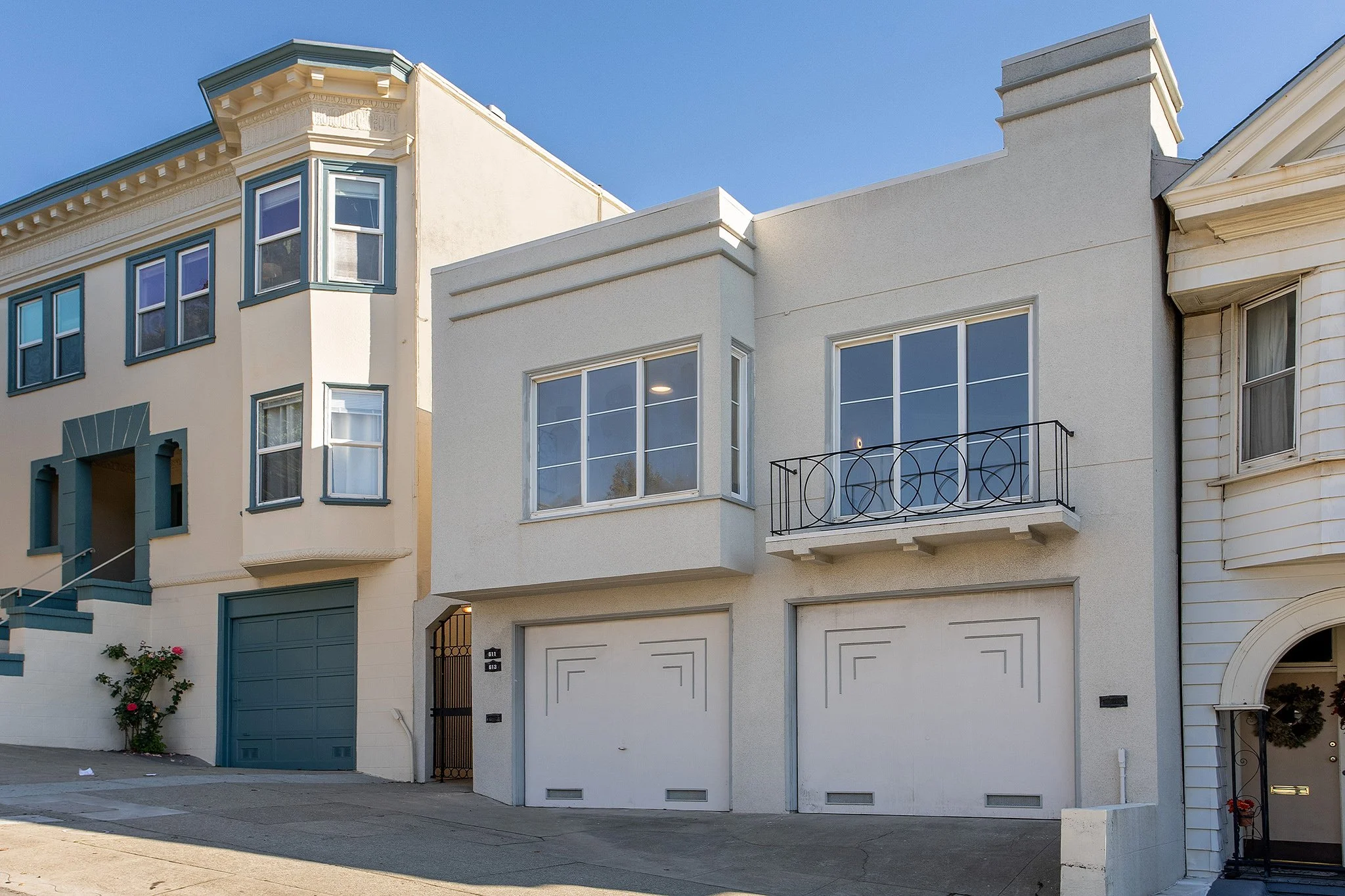 Front view of a modern residential building with a white facade, large windows, and two garage doors.
