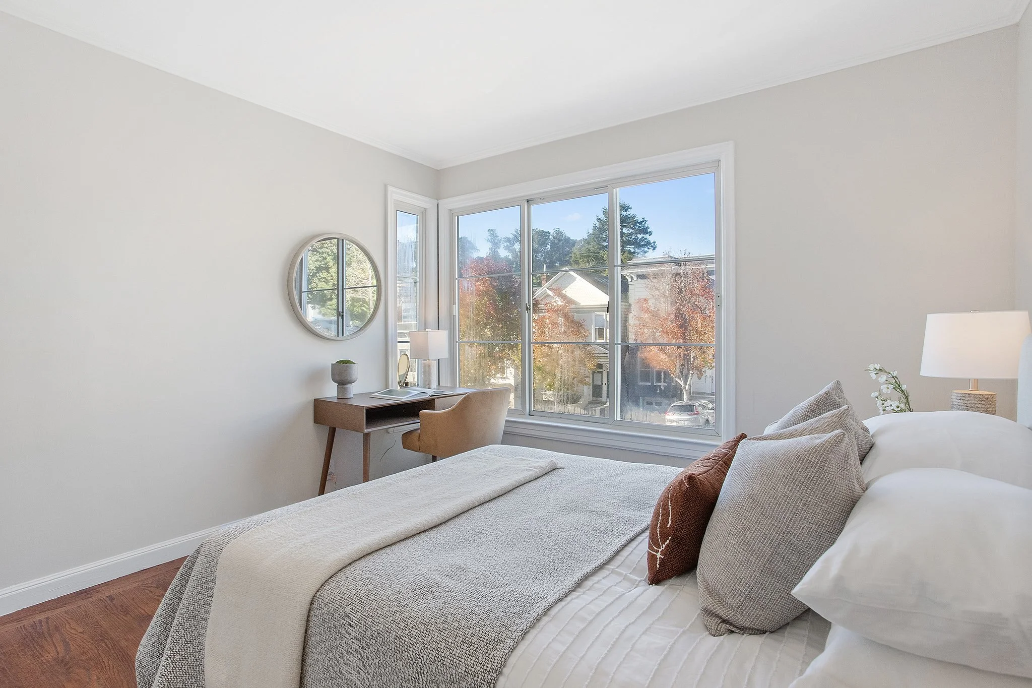 A bedroom with a bed, pillows, and a window showing trees and houses outside.