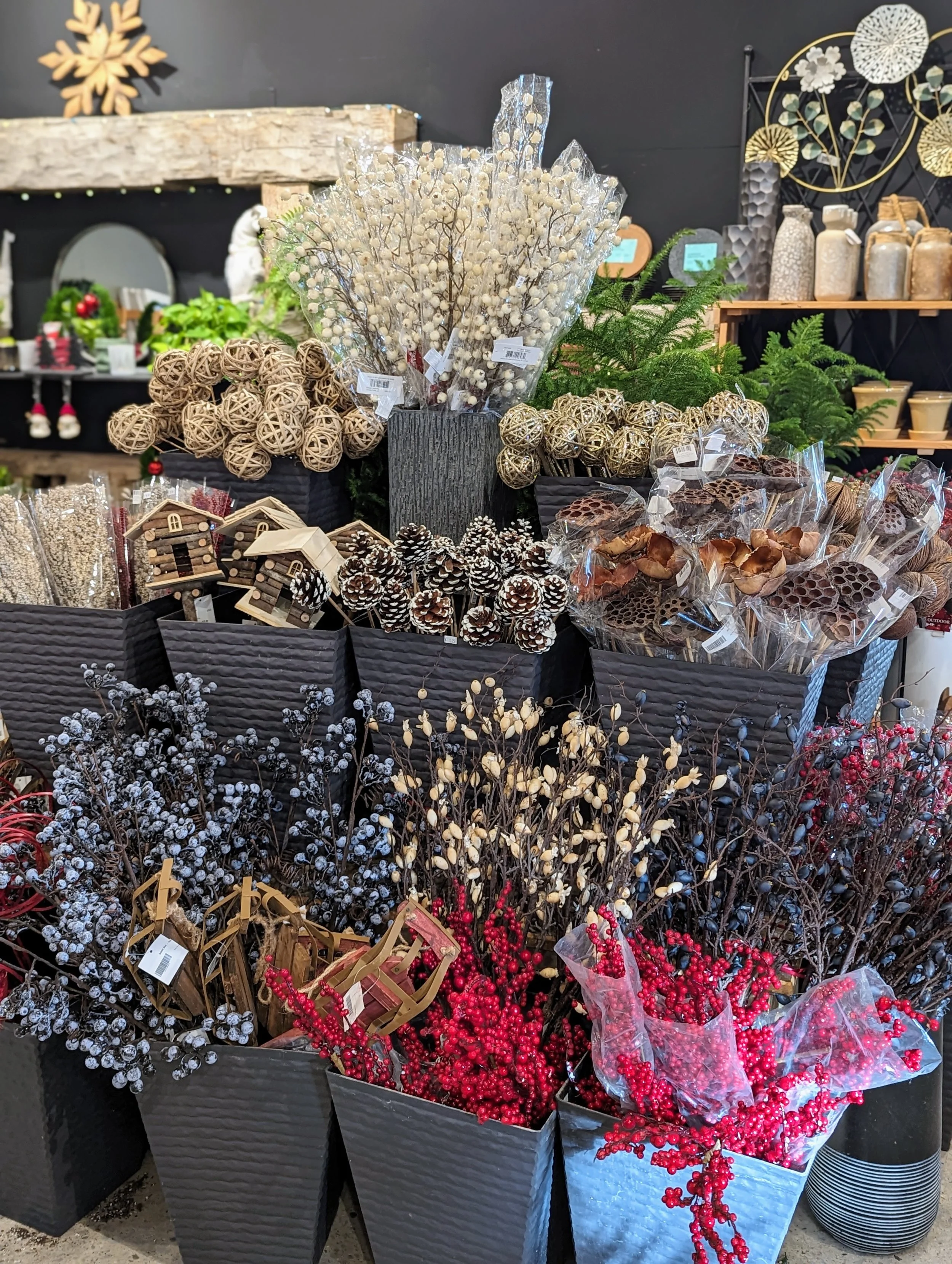 Display of holiday decorations and artificial plants including white, red, and beige berries, pinecones, and rattan balls at a store.