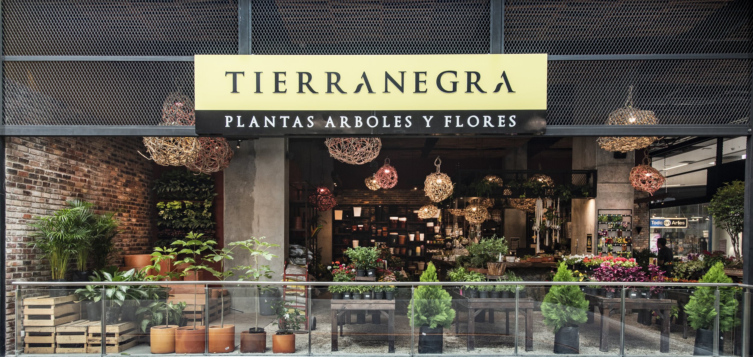 Fachada de una tienda de plantas y flores con señal que dice 'Tierranegra Plantas Árboles y Flores', exhibiendo plantas en el exterior y en el interior.
